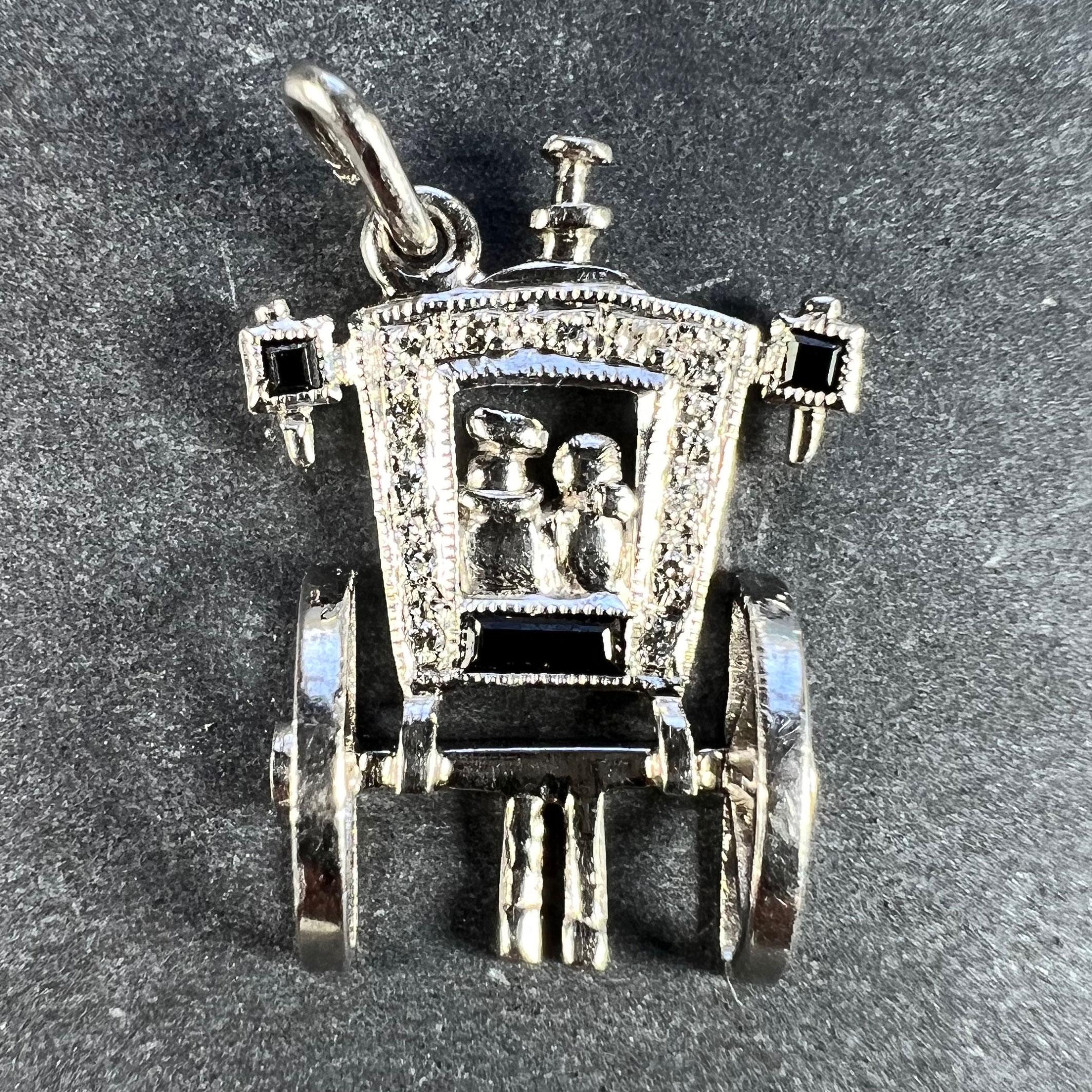 An Art Deco platinum charm pendant designed as a horse-drawn carriage viewed from behind, carrying a pair of newly weds. Set with emerald cut onyx to represent the Just Married panel and carriage lights, and 13 round brilliant cut diamonds with a