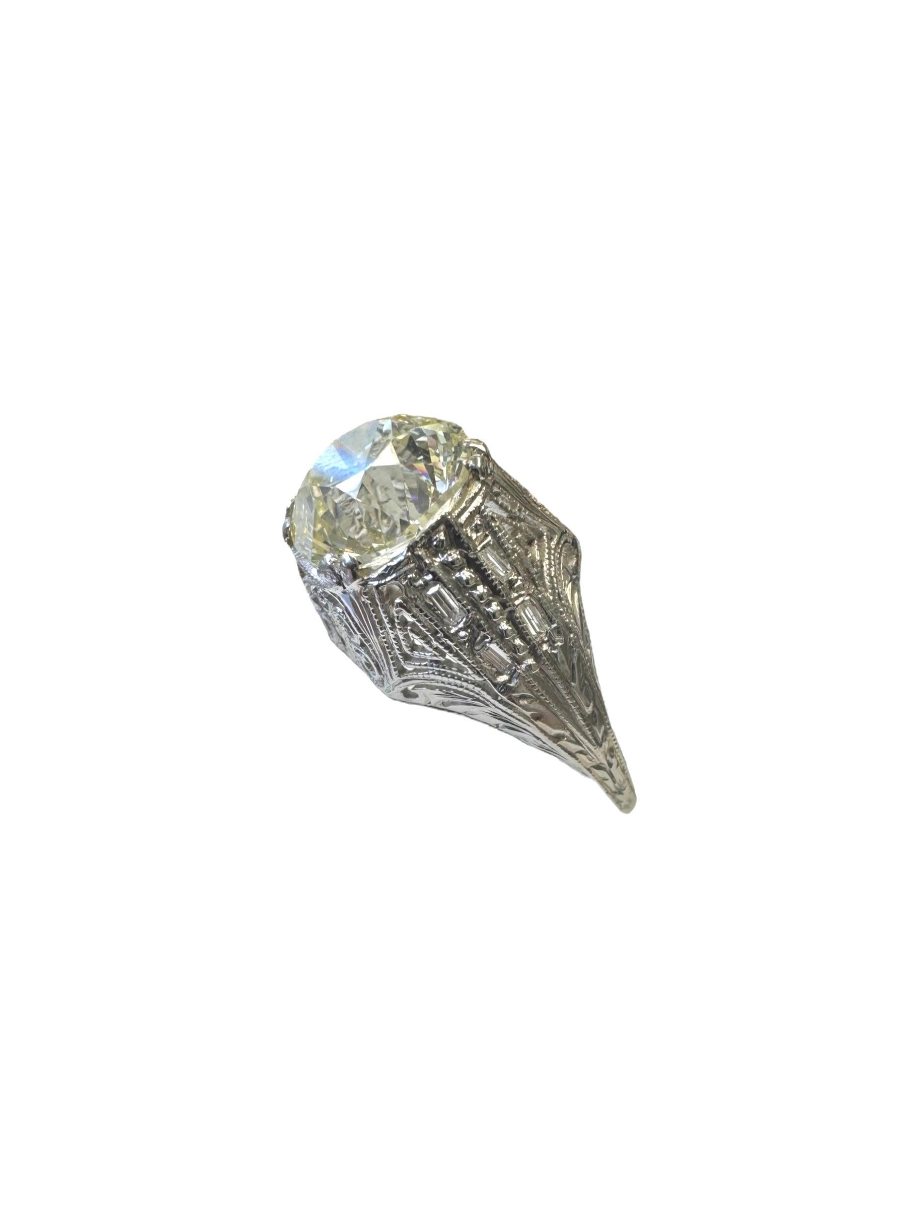 Excepcional anillo Art Decó de platino, centrado en un deslumbrante diamante talla mina antigua de 3,02 quilates, montado en un engaste finamente detallado y grabado a mano. La piedra central está flanqueada por diamantes talla baguette de