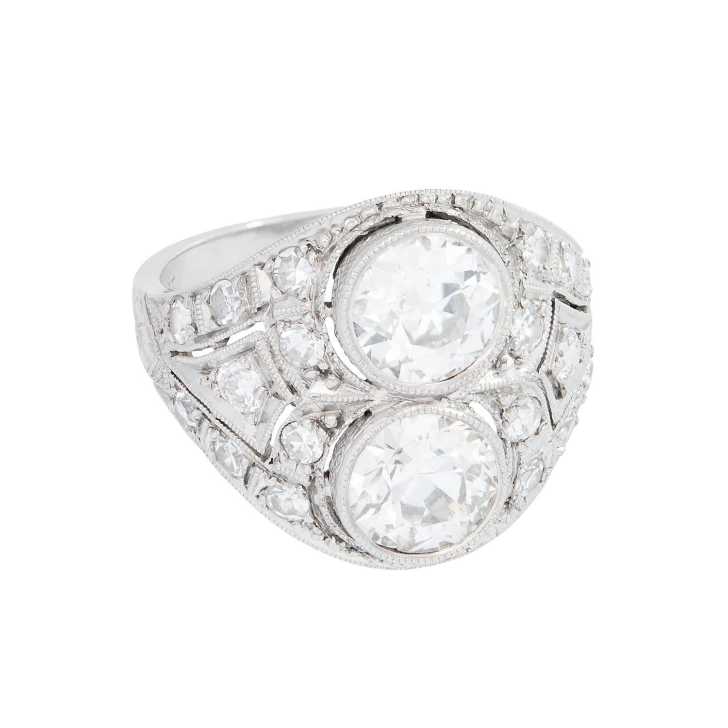 ¡Un cautivador anillo de diamantes que muestra una exquisita artesanía de la época Art Déco (1920)! Esta elegante pieza está elaborada en platino y presenta dos prominentes diamantes redondos engastados en bisel. Los diamantes están rodeados por una