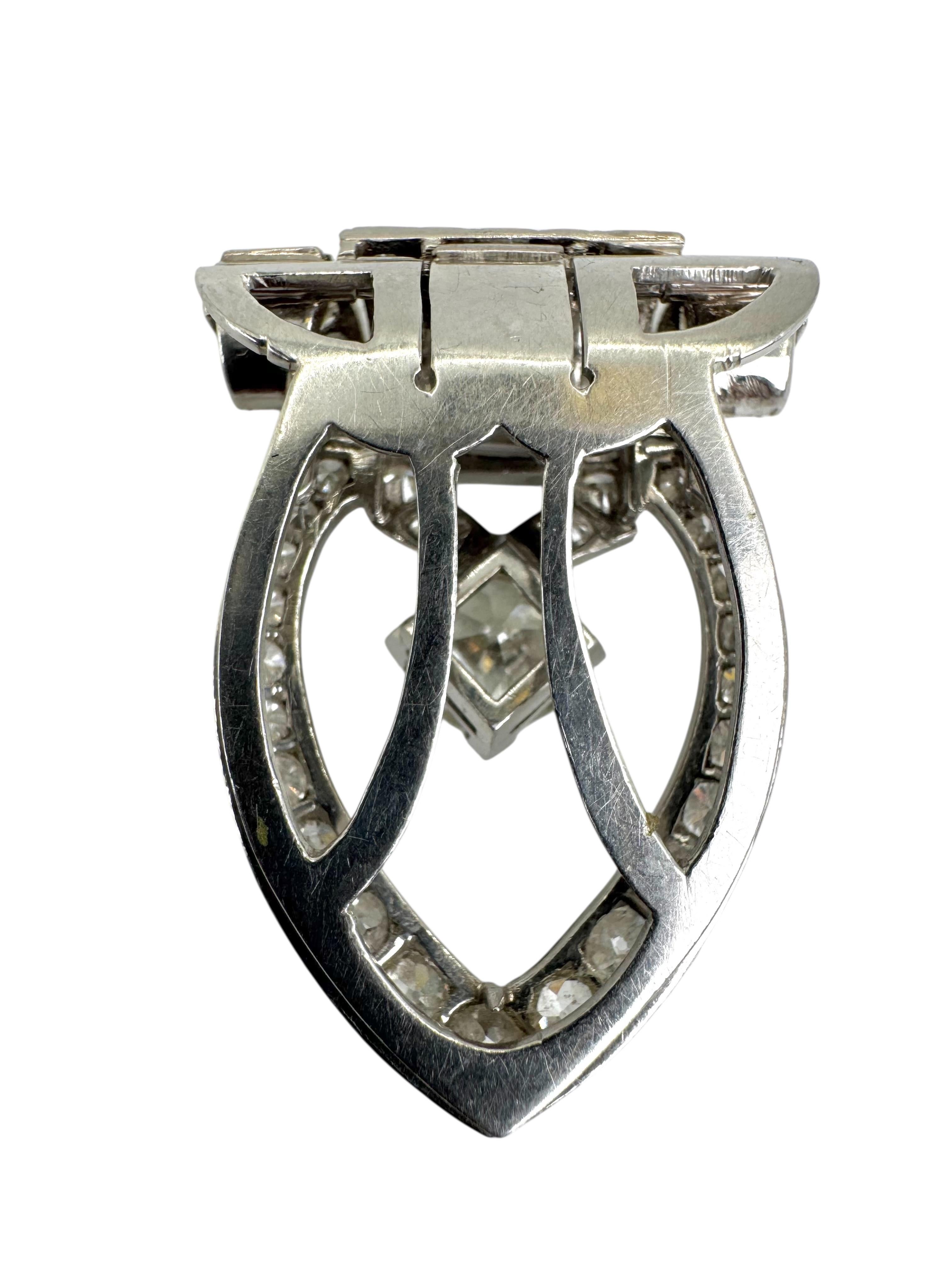 Un sorprendente fermaglio da abito in platino Art Deco, caratterizzato da un audace design architettonico incentrato su un vivace diamante di taglio europeo antico, di circa 1,25 carati, sospeso in una cornice a goccia aperta. La pietra centrale è