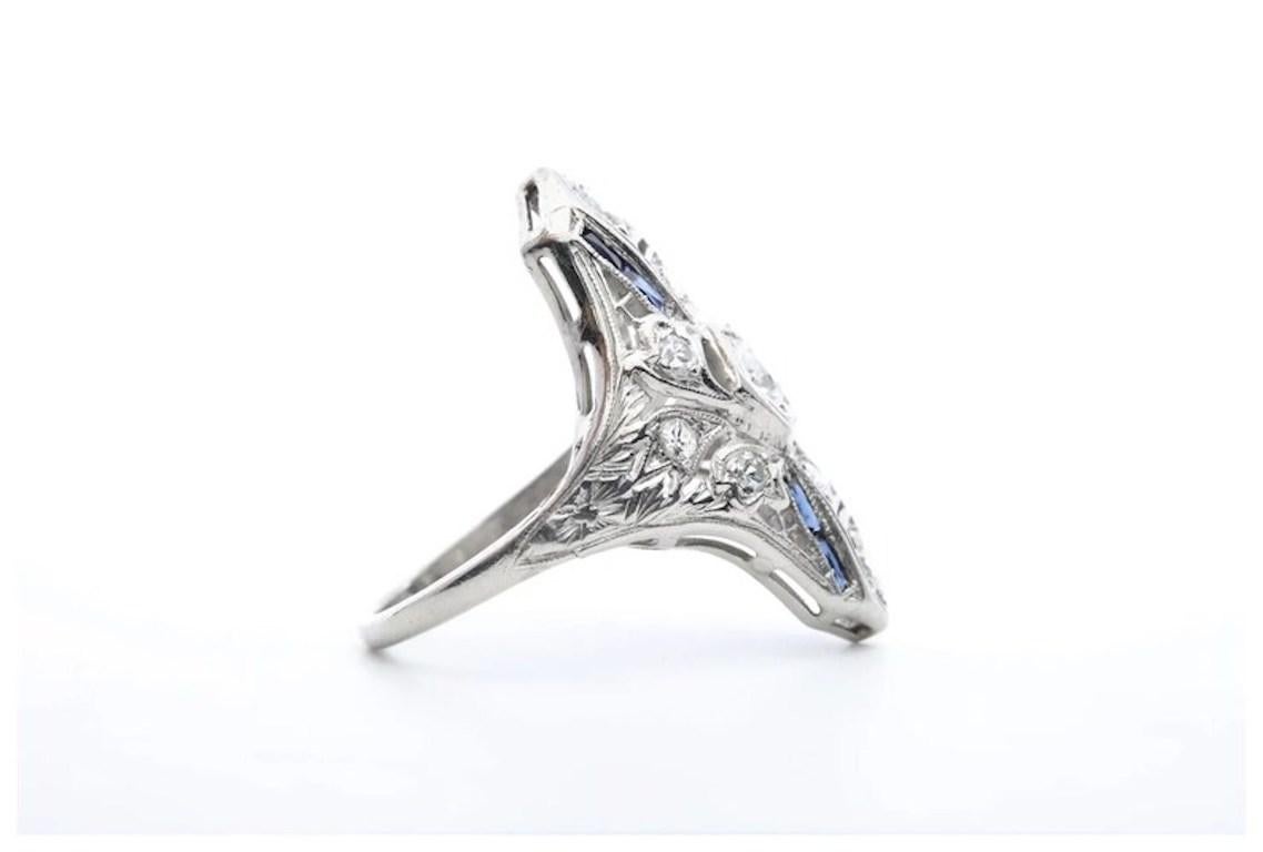 ston Estate Jewelry präsentiert:

Ein handgefertigter Art-Deco-Cocktailring aus Platin mit Diamanten und Saphiren. In der Mitte befindet sich ein 0,30 Karat schwerer Diamant im alten europäischen Schliff, der von zehn weiteren Diamanten in