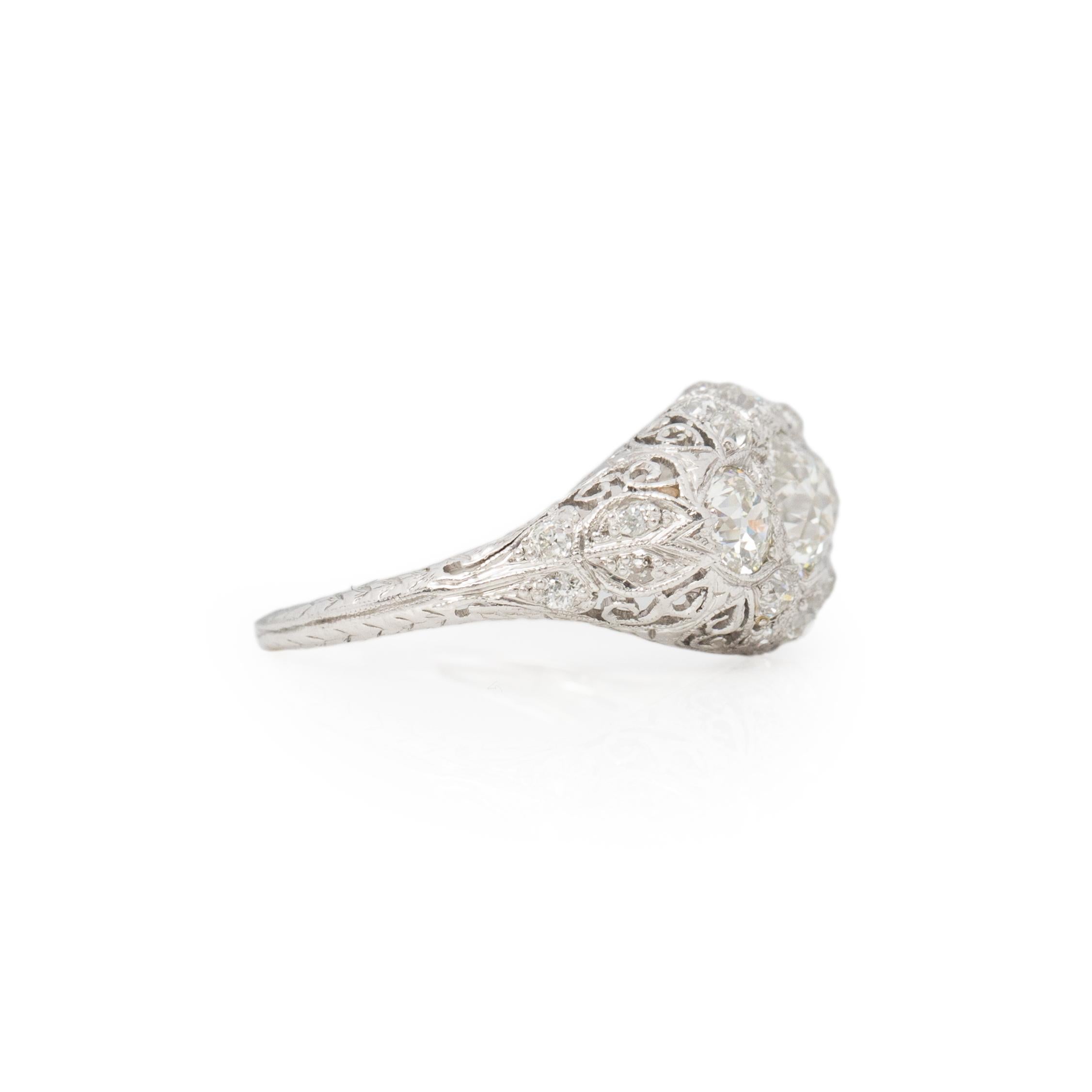 Here we have a stunning Art Deco piece, crafted in platinum. These three stone ring has outstanding filigree details, the delicate lace like design wraps around the diamonds giving the ring a weightless feel. In the center is a near one carat old
