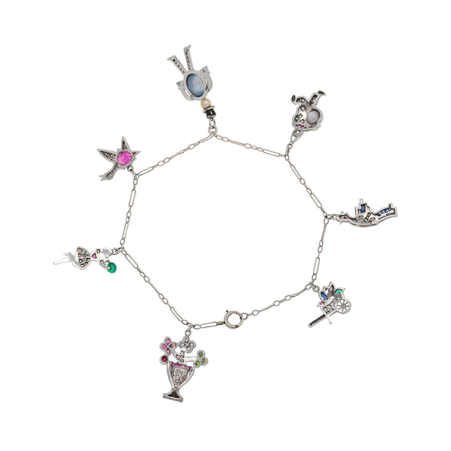 A beautiful charm bracelet from the Art Deco (ca1920) era! This lovely piece is a wonderful compilation of 7 charms that dangle from a fine platinum chain bracelet. Each platinum charm is unique and all are detailed with different sparkling