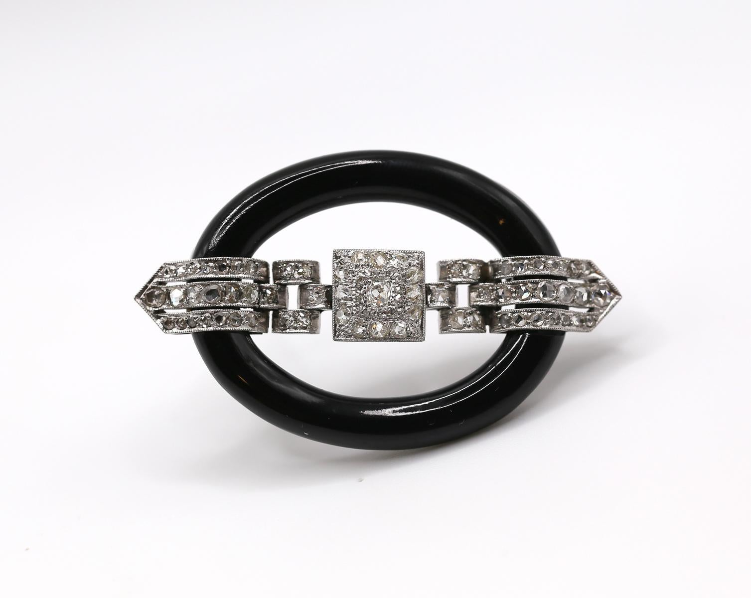 Iconic Art Deco design. Platinum top and Gold brooch adorned with Diamonds featuring Onyx oval. Reminiscent of a buckle.

Black Onyx and Old mine and Rose-cut Diamonds. 
Platinum and white gold. 2 1/4 x 1 3/8 inches.
Characteristics Color: G-J.

So