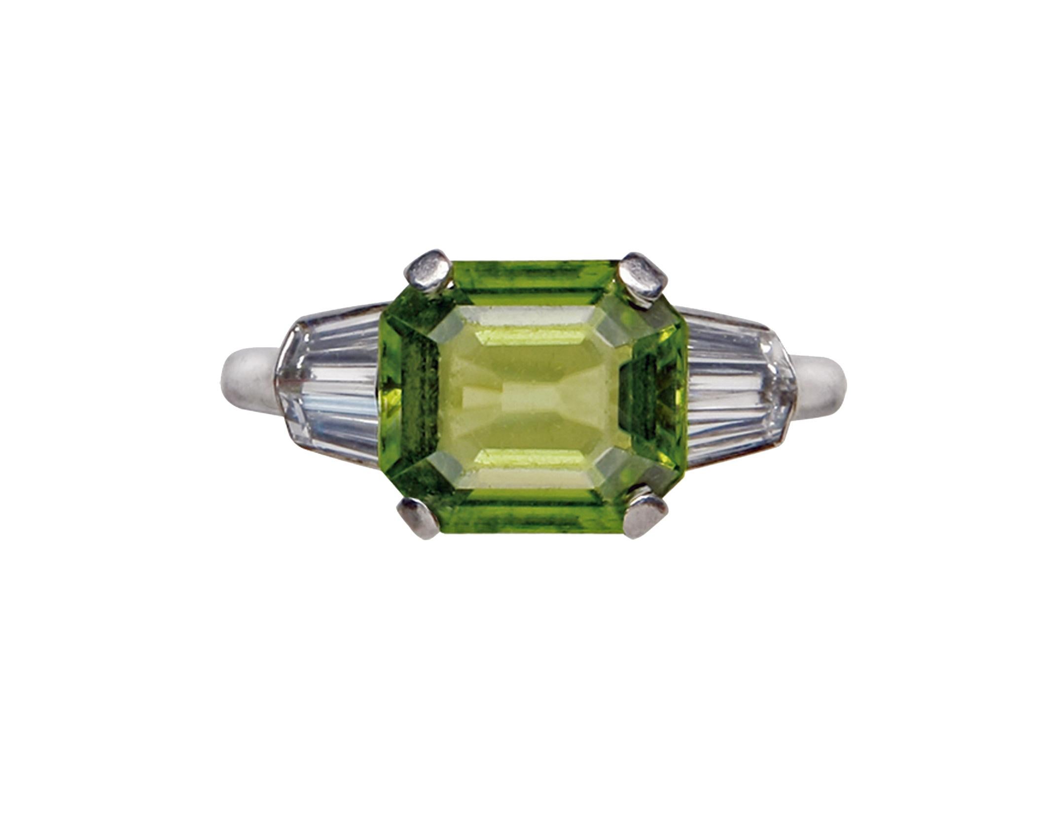 Art Deco Platinum Peridot Diamond Ring, C.1920. The Ring set with an emerald cut Peridot, gauging 9.40 x 8.30 x 4.65 mm, approximately 3.00 cts, flanked on either side with three tapered baguette cut diamonds, total diamond weight approximately 0.90