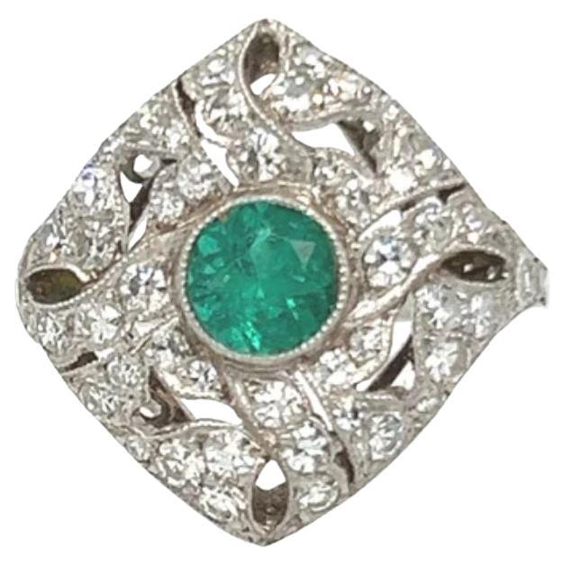 This stunning Art Deco ring highlights a vibrant round-cut emerald at its center, framed by intricate platinum filigree adorned with sparkling diamonds. Designed in the 1920s to 1930s, this piece embodies the geometric elegance and bold artistry of