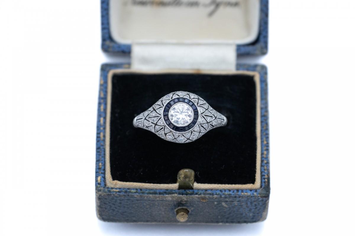 Antique Art Deco ring with diamonds and sapphires.

The platinum ring is decorated with a main diamond weighing 0.45ct and 50 side diamonds. Additionally, the ring is decorated with 19 dark blue carre-cut sapphires.

The beautiful openwork geometric