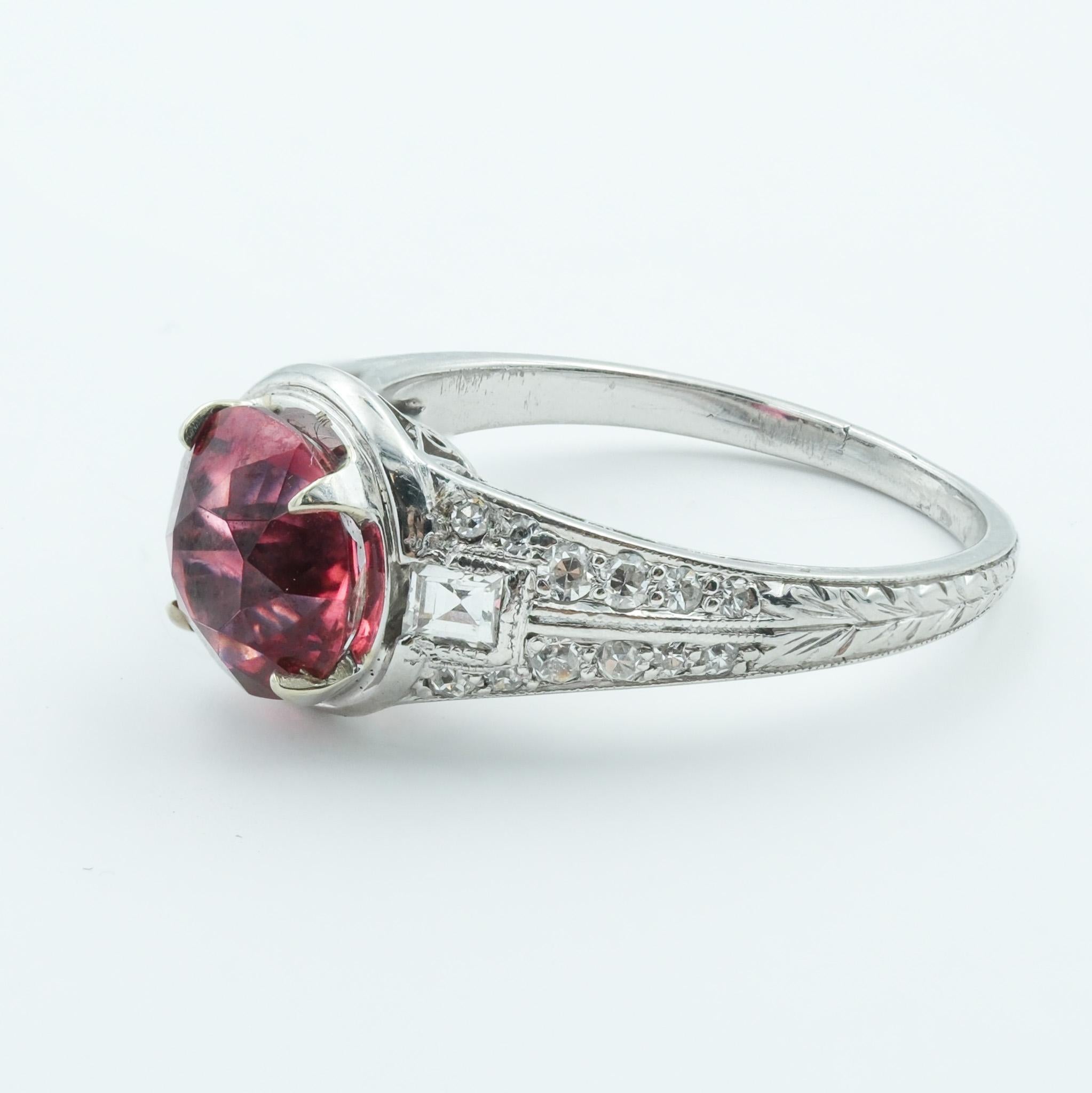 This ring is a stunning piece of Art Deco jewelry, crafted from fine platinum and set with a magnificent 2.07ct natural spinel as the centerpiece. The spinel, known for its deep red color that can rival the ruby, is cut in a round shape that