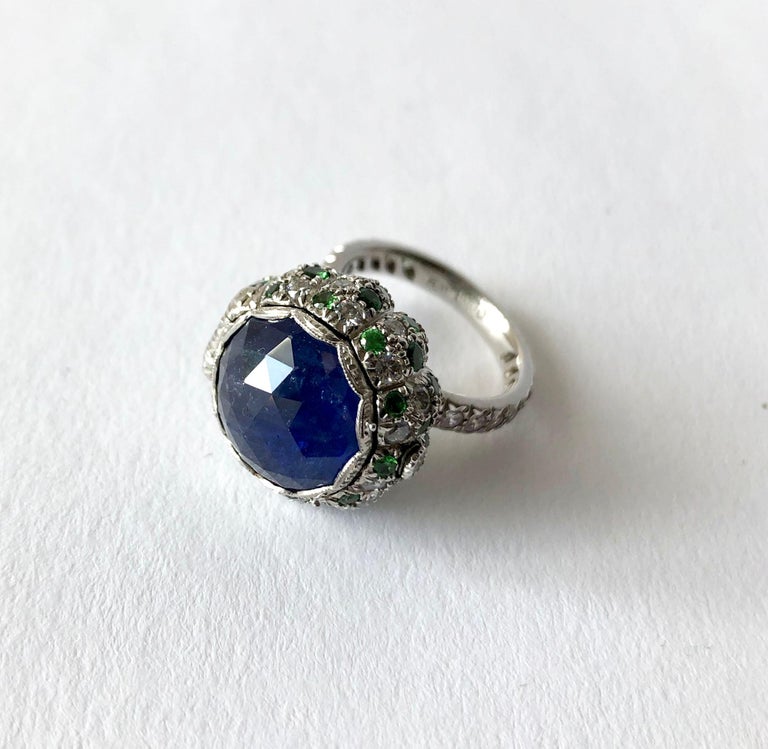 Platinum pill box ring with large antique rose cut blue sapphire, emeralds and diamonds, possibly European.  Diamonds also embellish the shank halfway.  Sapphire lid opens by two prongs located on the side, interior of the box has a gold was finish.