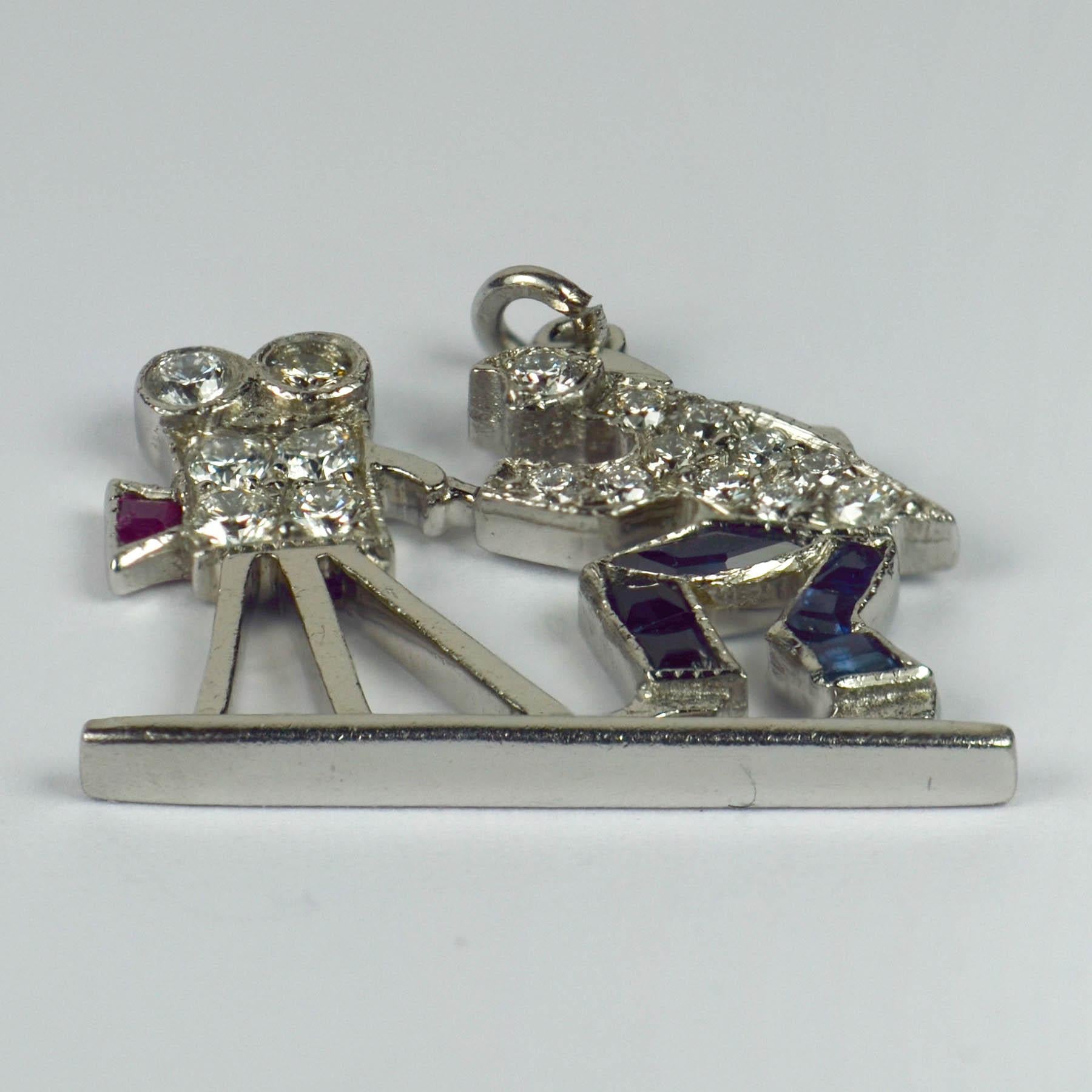 An Art Deco platinum charm pendant designed as a Hollywood cameraman behind a film camera set with 17 round brilliant cut diamonds, six step cut blue sapphires and a step cut ruby. Unmarked but tested as platinum. 

Estimated total gem weights: