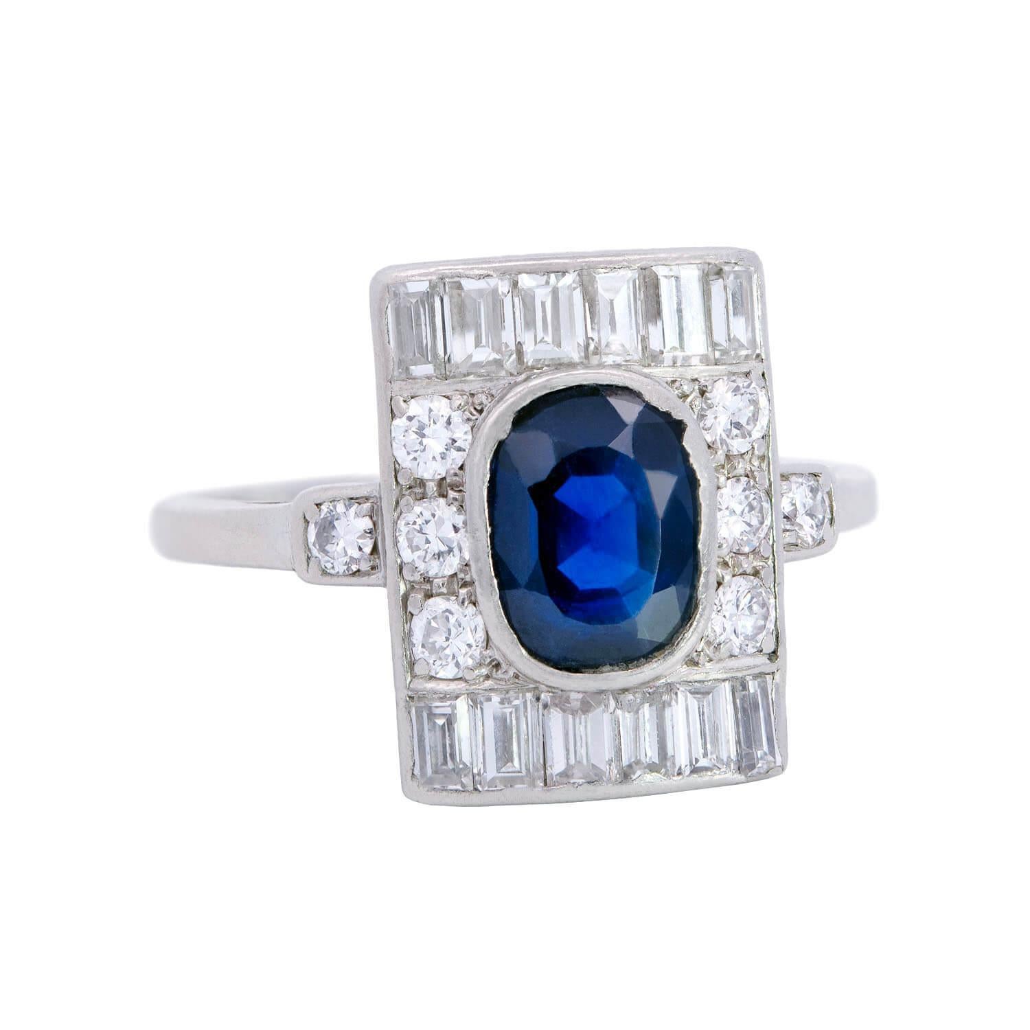 Une superbe bague en saphir et diamant inspirée de l'époque Art déco ! Cette magnifique bague est fabriquée en platine et contient un superbe saphir de taille ovale au centre, contenu dans un chaton ouvert. La pierre centrale est entourée d'un