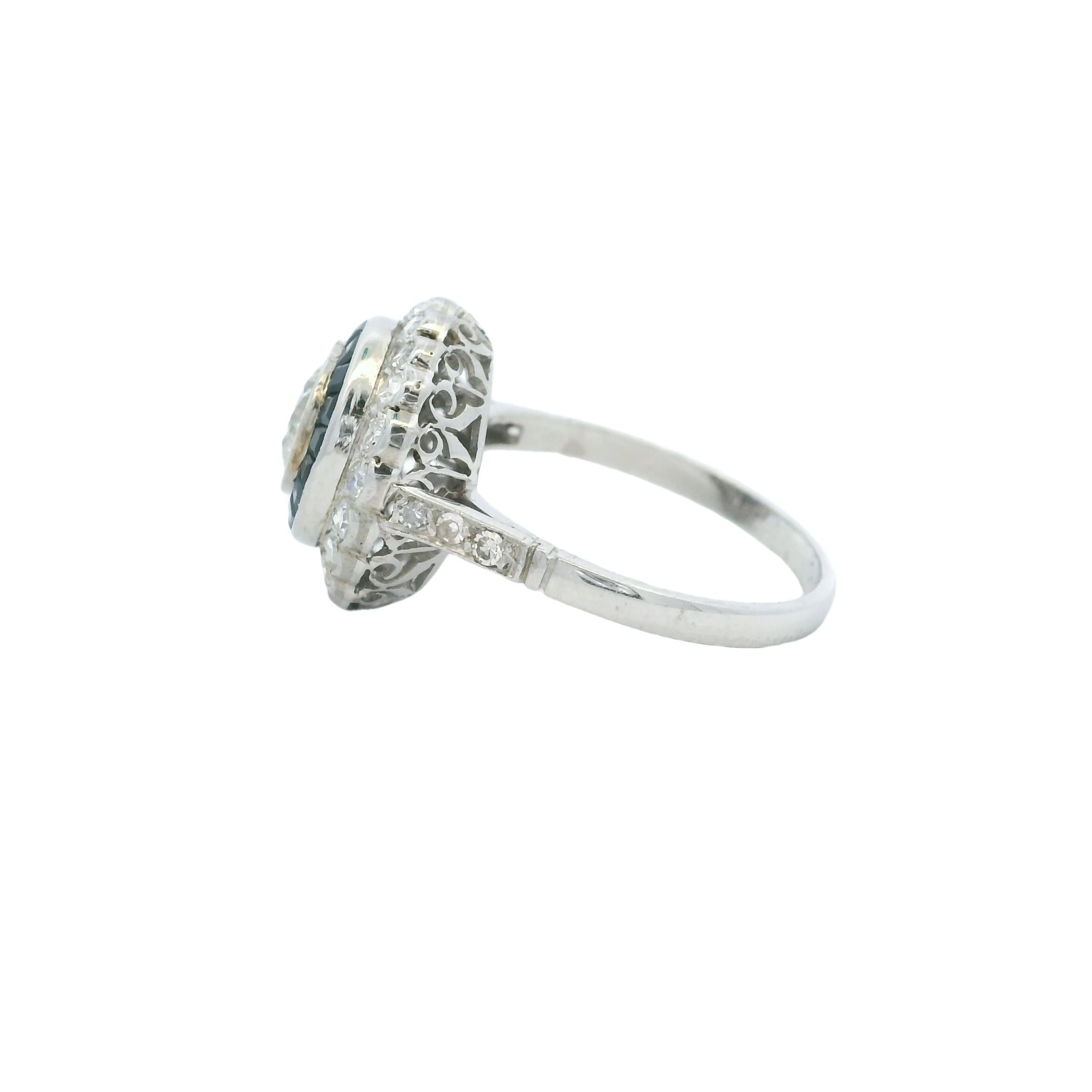 This vintage platinum engagement ring captures the elegance of the Art Deco era with a bold double halo design. At its center sits a round brilliant-cut diamond weighing approximately 1.20 carats (H color, VS clarity), bezel-set and surrounded by a
