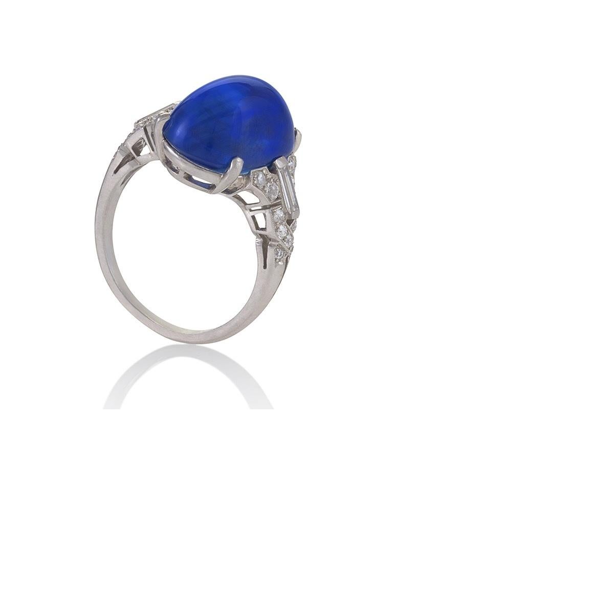 This substantial cabochon blue sapphire and diamond ring is a beautiful example of Art Deco opulence. Elegantly proportioned and reminiscent of architectural splendor, the graceful gem is flanked by delicate openwork shoulders enhanced by round- and