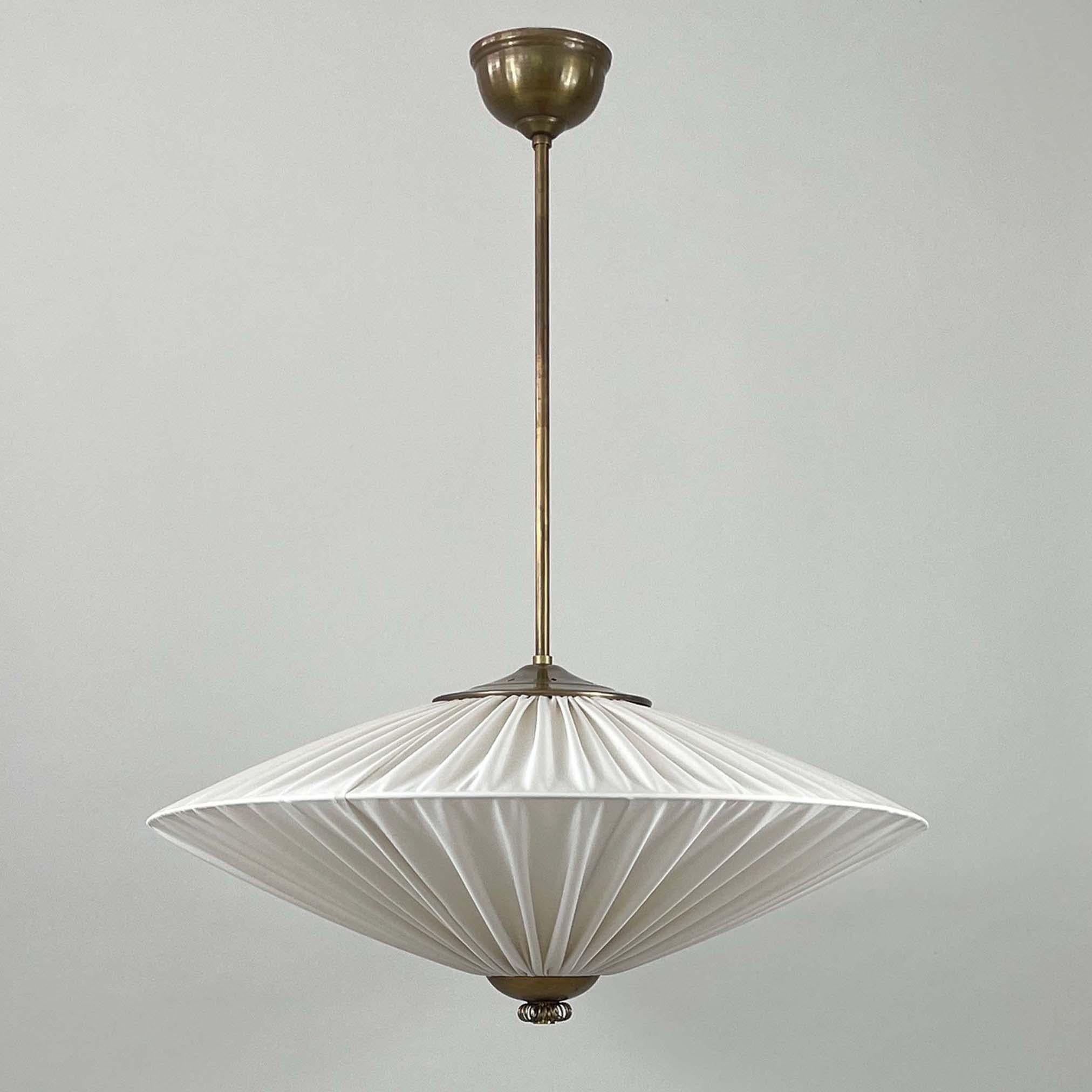 This elegant Art Deco pendant was designed and manufactured in Finland in the 1940s. It features a large light cream (off-white) colored pleated fabric lampshade and brass hardware.

The shade has a symmetrical, slightly convex shape that tapers at