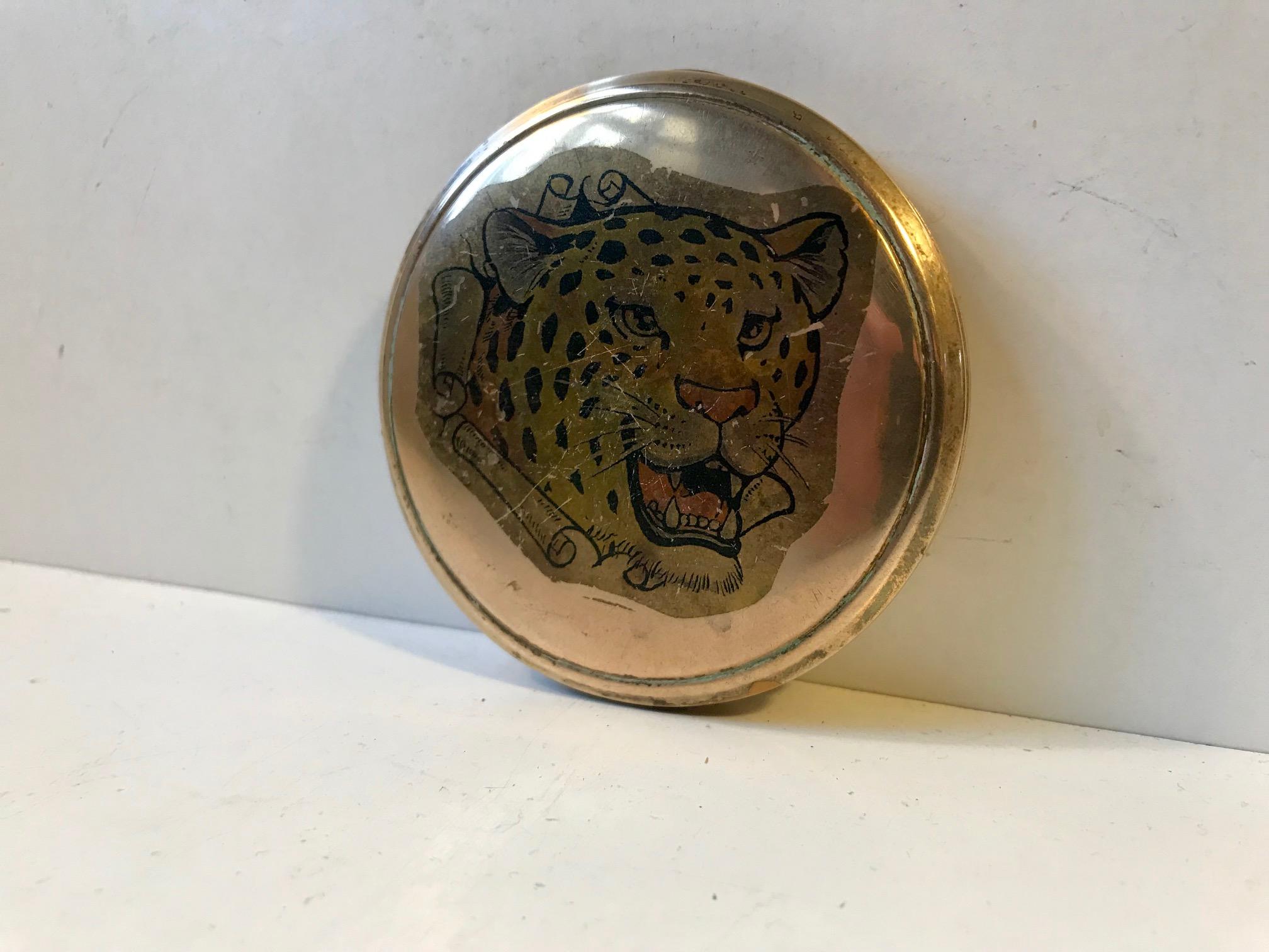 A powder compact or pocket mirror also suitable for pills, snuff etc. It is fashioned out of solid brass and has a front with intricate Guilloché. Both the front and backside has a tiger motif created through a process with different acids, leaving
