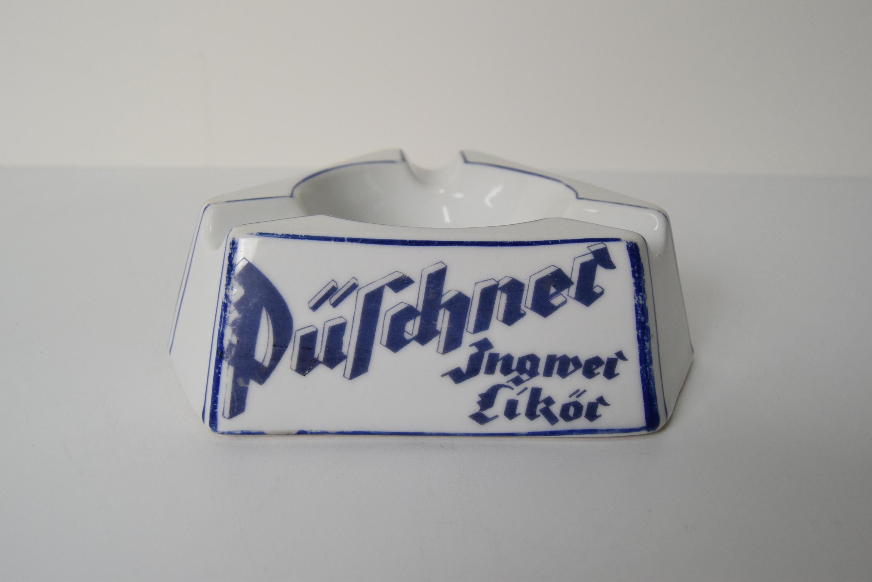 Posacenere pubblicitario in porcellana Art Deco Püschner Bitter, anni '20.
Il posacenere è decorato con iscrizioni incorniciate in blu con scritte stilizzate
Presenta segni di utilizzo
 Un originale oggetto da collezione, adatto ad arricchire una