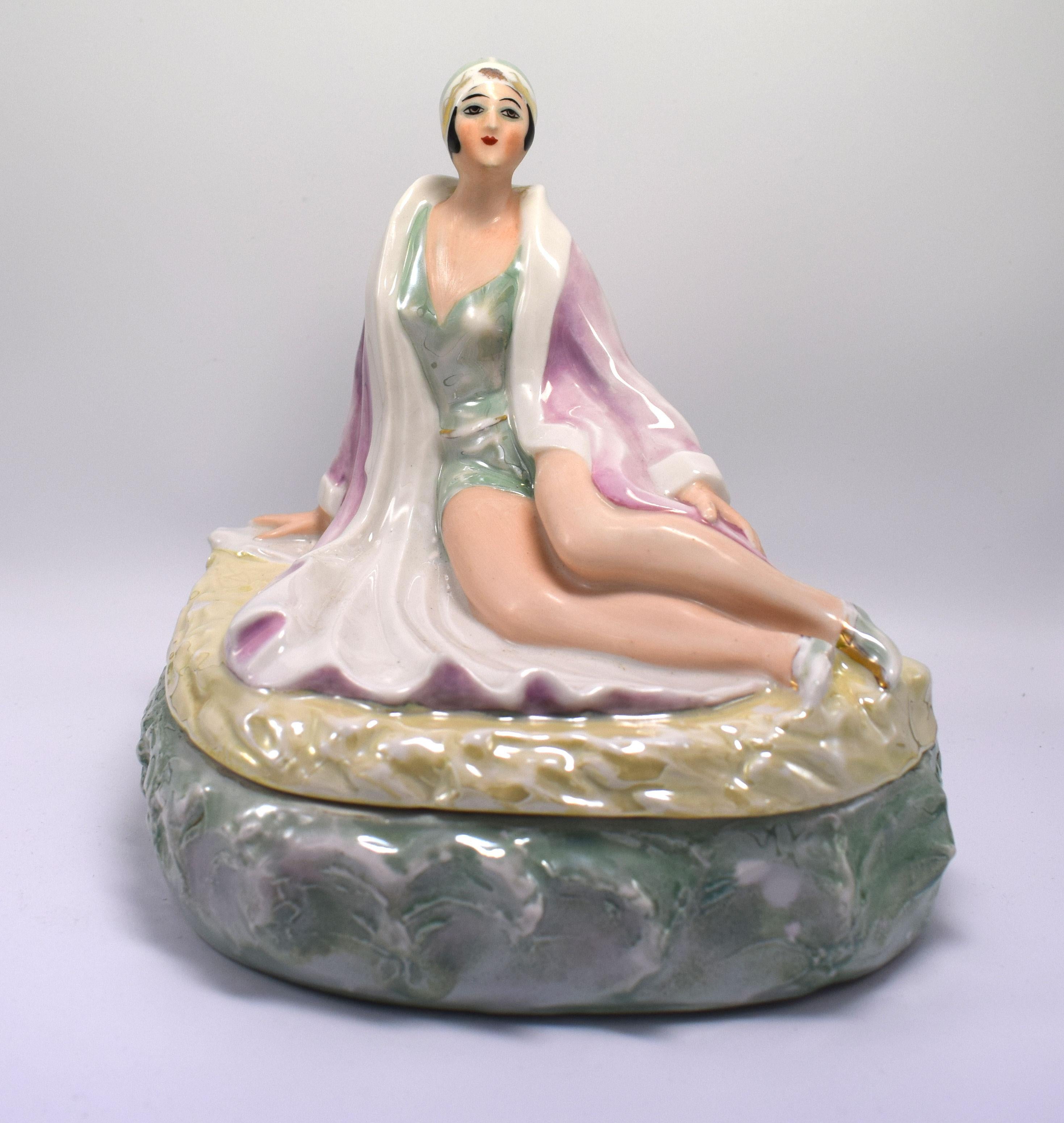 Fantastic original Art Deco porcelain box of a bathing beauty flapper girl. Made of porcelain and finished with lustre glazes, she has an exquisite face and is modelled as if lying on a beach (the lid) surrounded by waves (the base of the box).