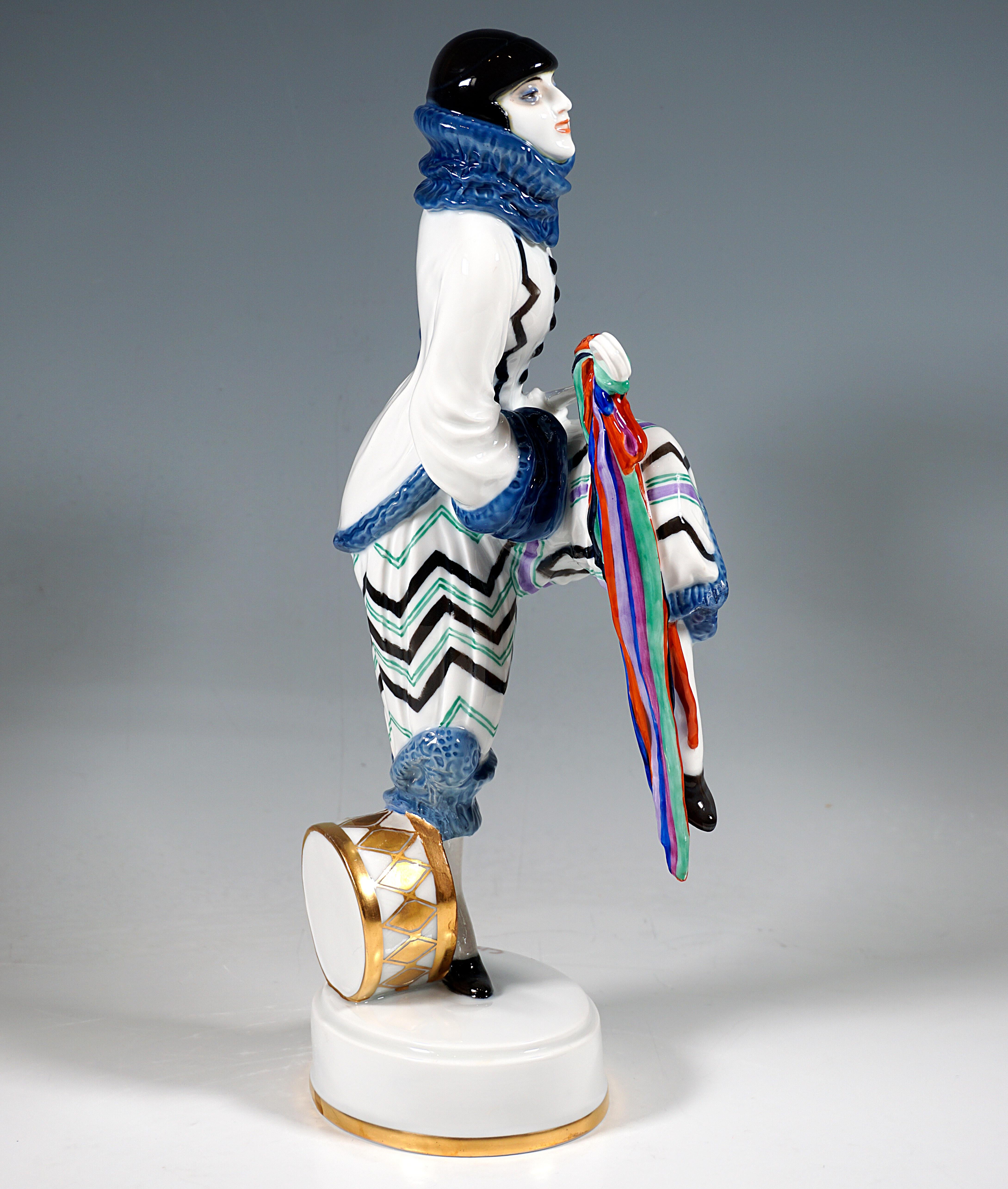 Very rare Porcelaine Figurine after the dancer Lena Amsel:
Dancer in an exotic Pierrot costume with a zigzag pattern, with large flounced cuffs and matching high collar, posing in marching step with one leg raised and playing a lute with a long