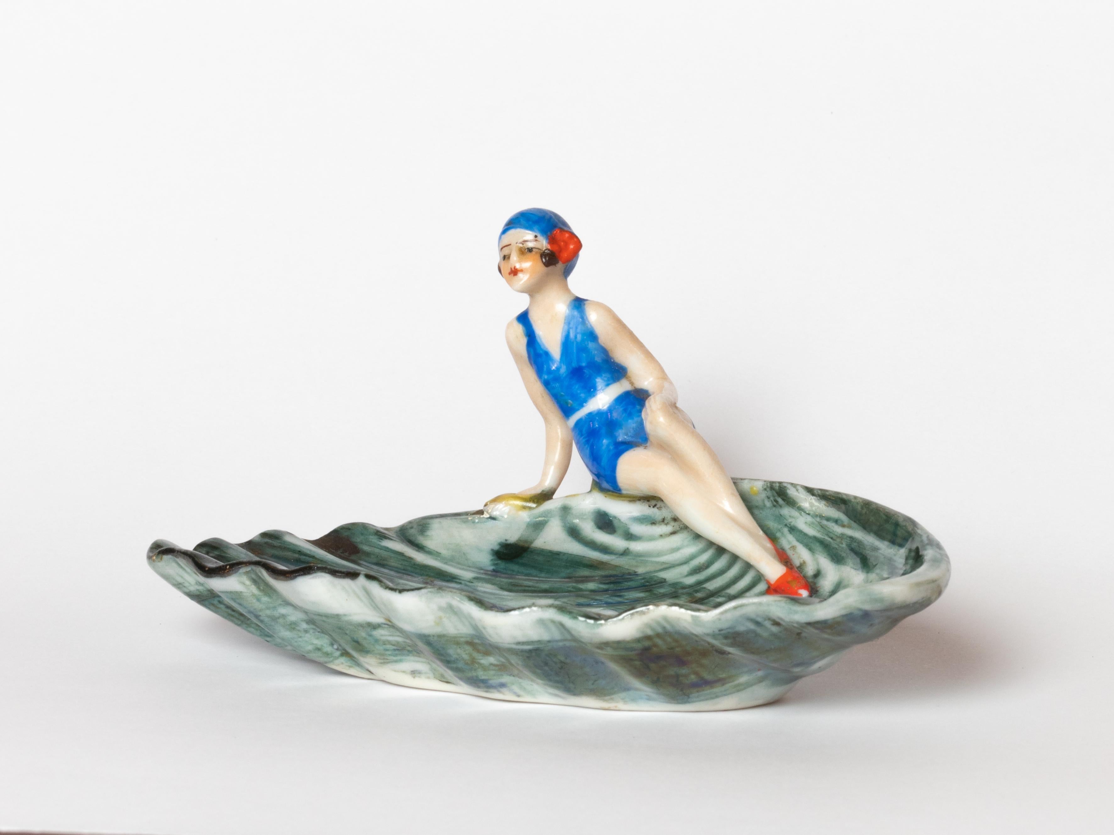 This Art Deco porcelain figurine from 1929, crafted by W. Goebel in Rodental, Bavaria, features a refined pin-up figure with a nacre-like finish. The miniature sculpture stands out for its delicate modeling and elegant posture, inspired by the
