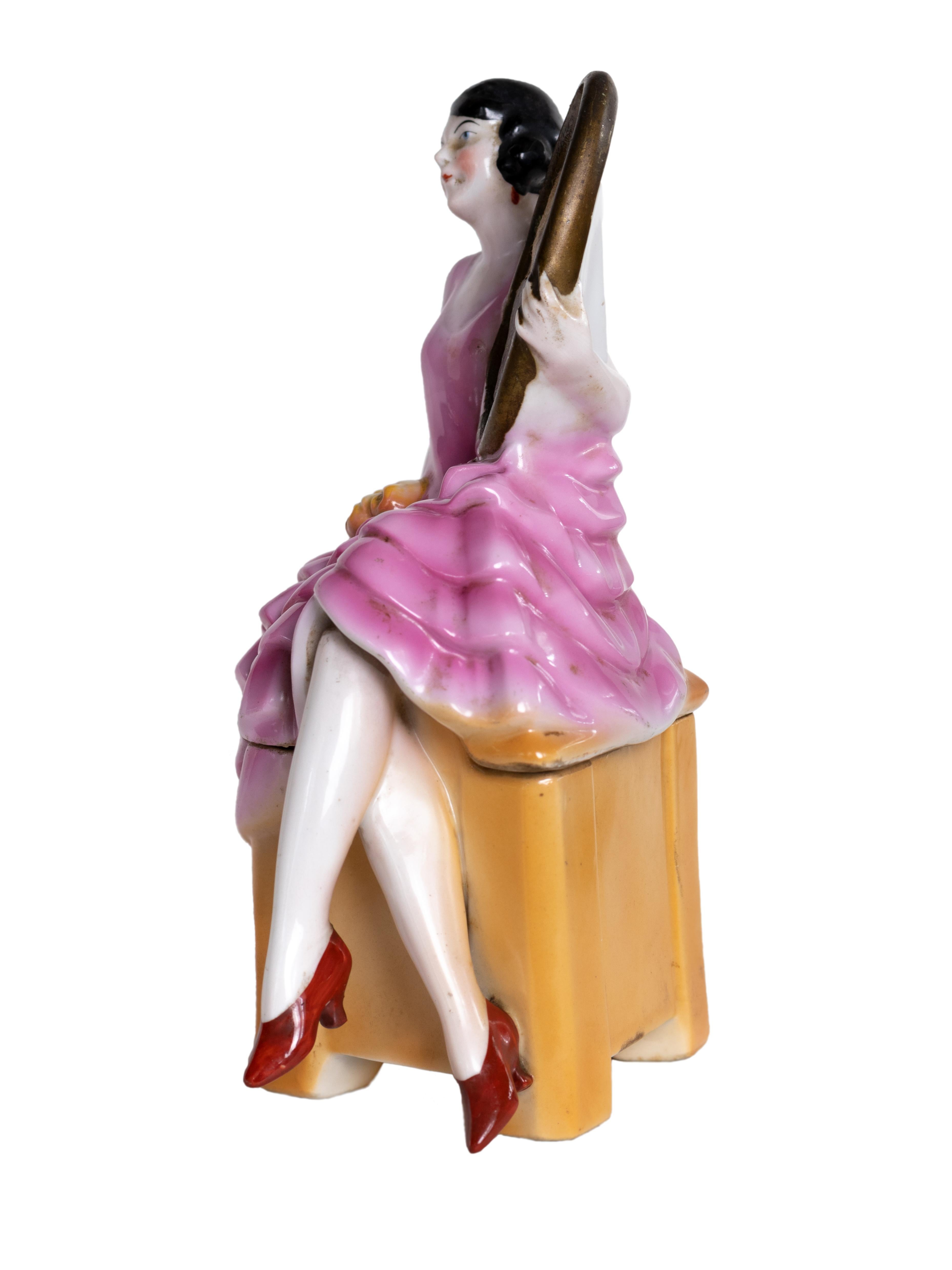 Boîte à poudre en porcelaine Art déco des années 1930, représentant une femme assise dans une robe rose à volants tenant un miroir ovale. Ce meuble-lavabo en deux parties illustre l'élégance et le glamour de l'entre-deux-guerres, évoquant la culture