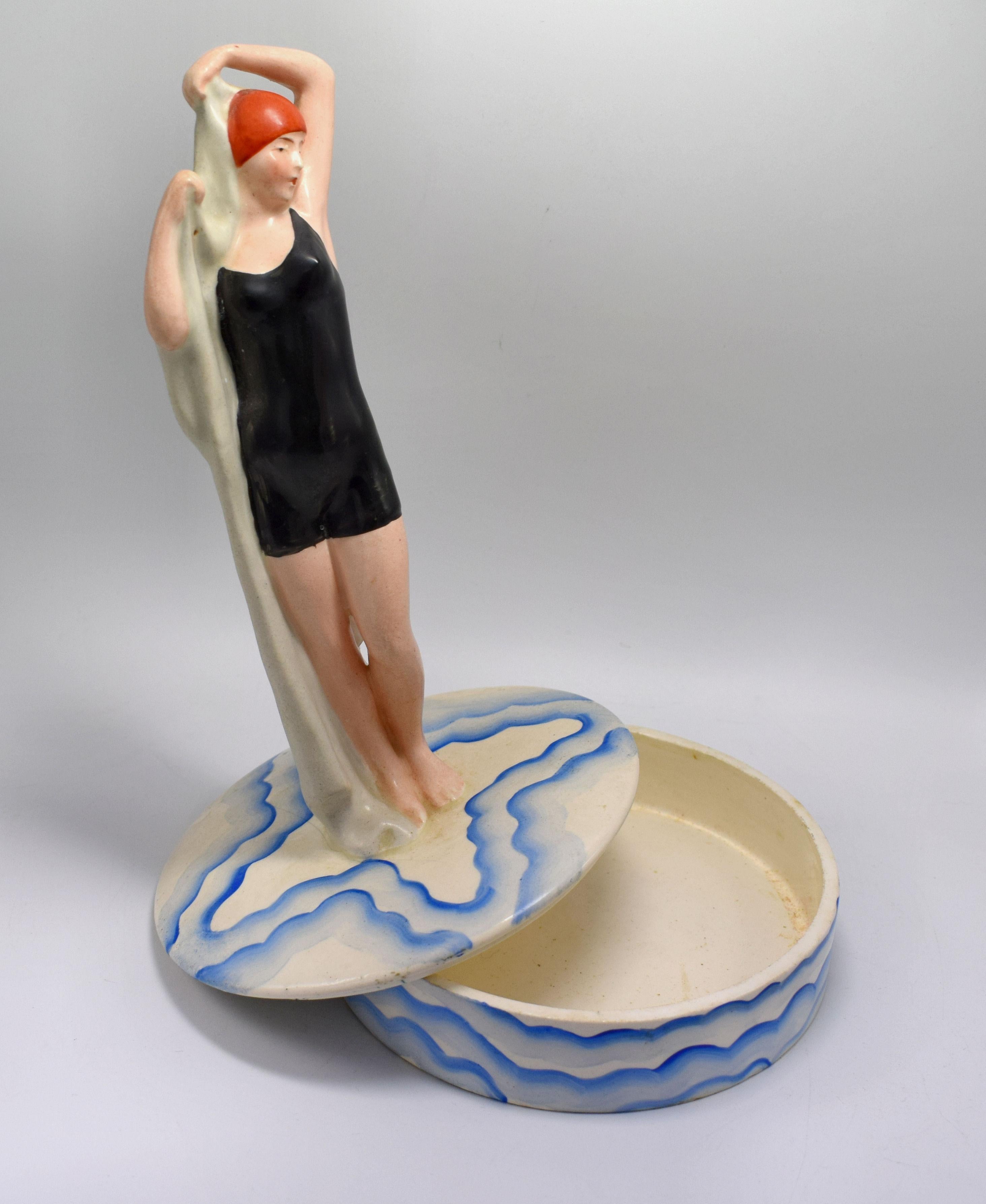 For your consideration is this rare and very enchanting ceramic powder / trinket box, dating to the 1930s, sourced in US. Depicts a flapper girl stood drying herself with a bath towel dressed in the fashion of the day bathing costume. The base,