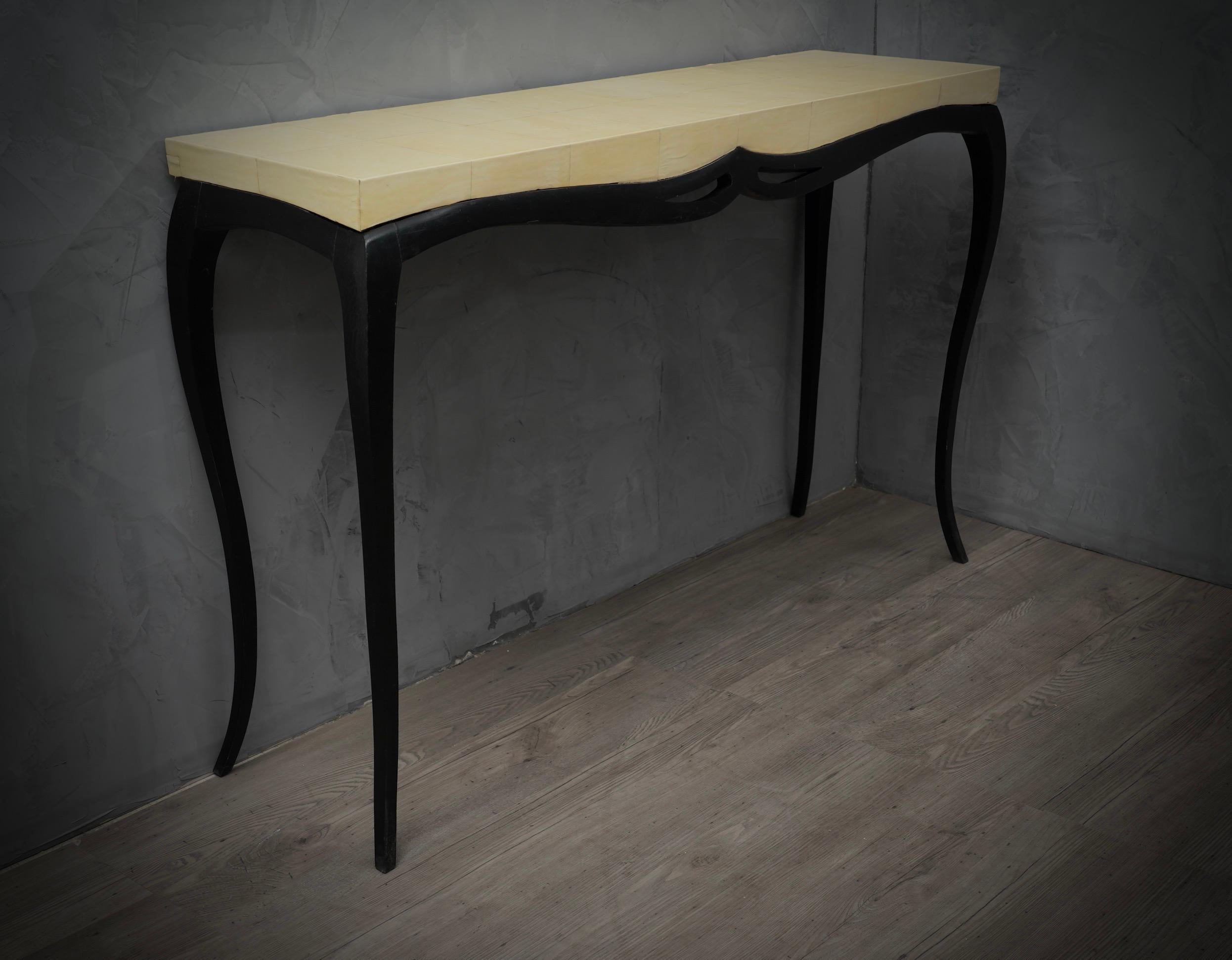 Diese sehr bewegungsreiche Konsole ist einzigartig in ihrer Art, auch wegen des kostbaren Materials, mit dem sie beschichtet ist.

Die Konsole besteht aus einer mit Ziegenleder überzogenen Holzplatte, wobei das Leder auch einen Teil der Seitenkante