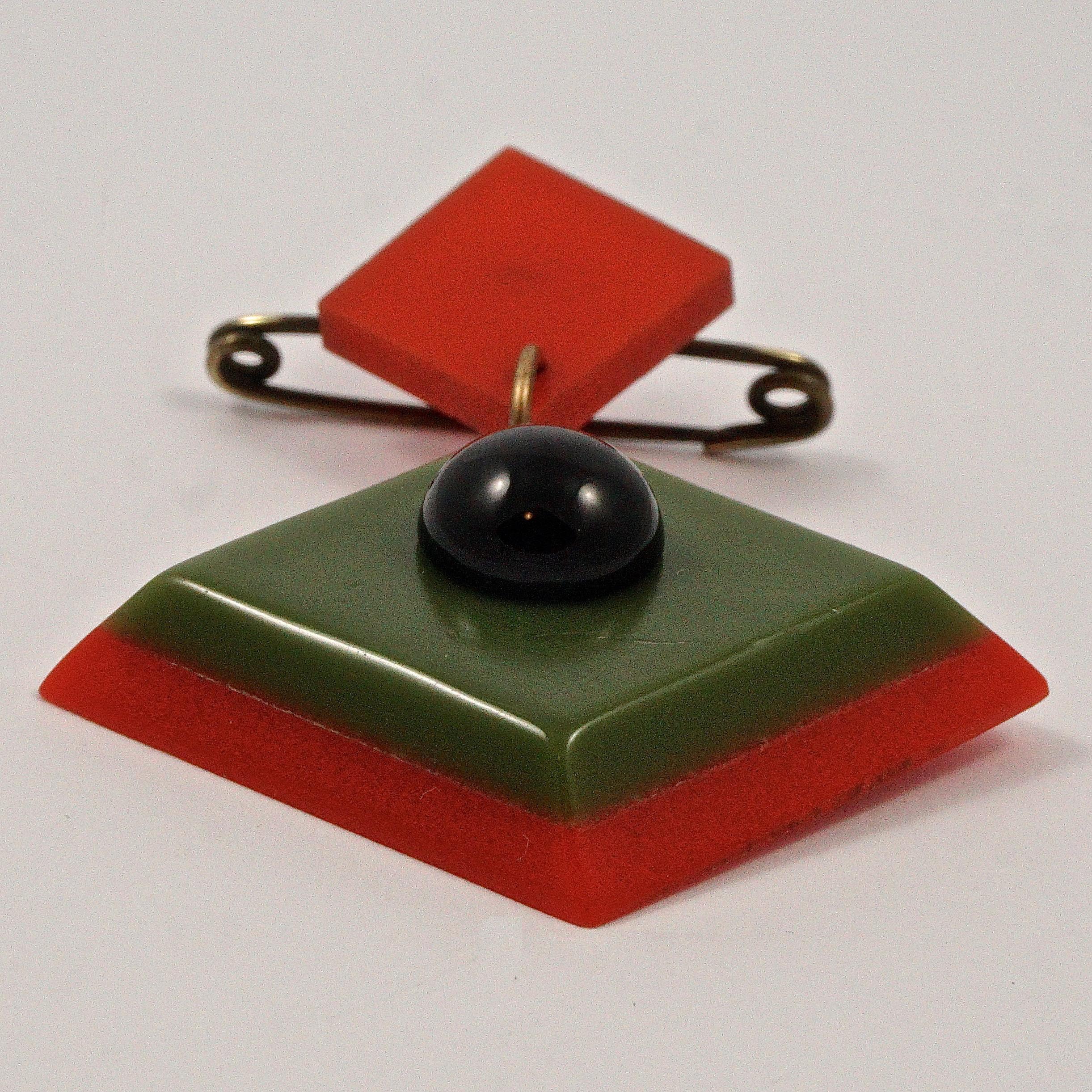 Wunderschöne geometrische Art-Déco-Brosche mit roten und grünen Kunststoffquadraten und einer schwarzen Glaskuppel. Messlänge 6,1 cm / 2,4 Zoll bei maximaler Breite 4,45 cm / 1,75 Zoll. Die Brosche ist in sehr gutem Zustand, mit einigen