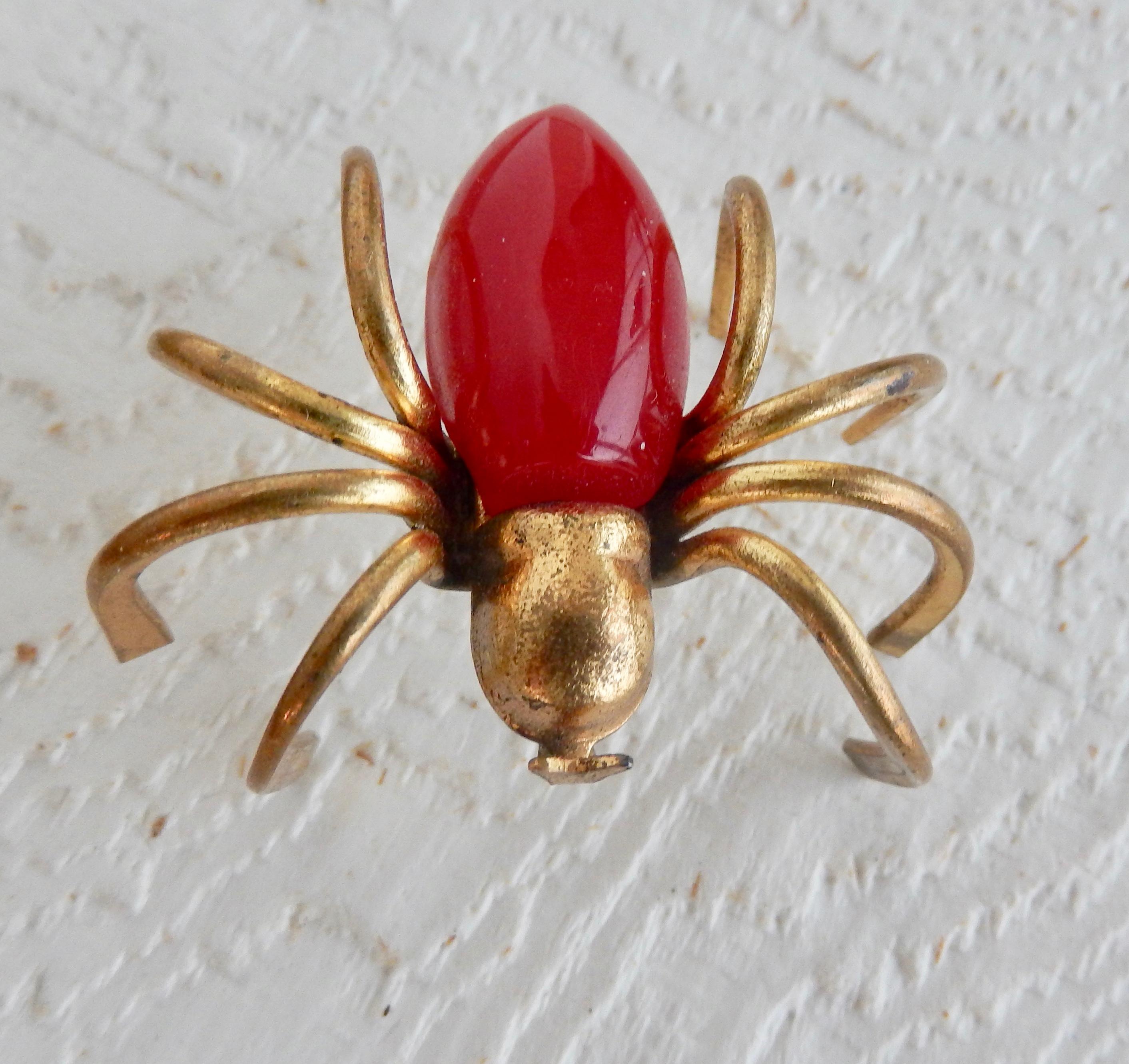 A whimsical three-dimensional gilt metal spider pin with a red bakelite body from the 1940s. In very good condition. A classic, scarce example of American Art Deco costume jewelry. 

A similar brooch, listed separately, is available with orange