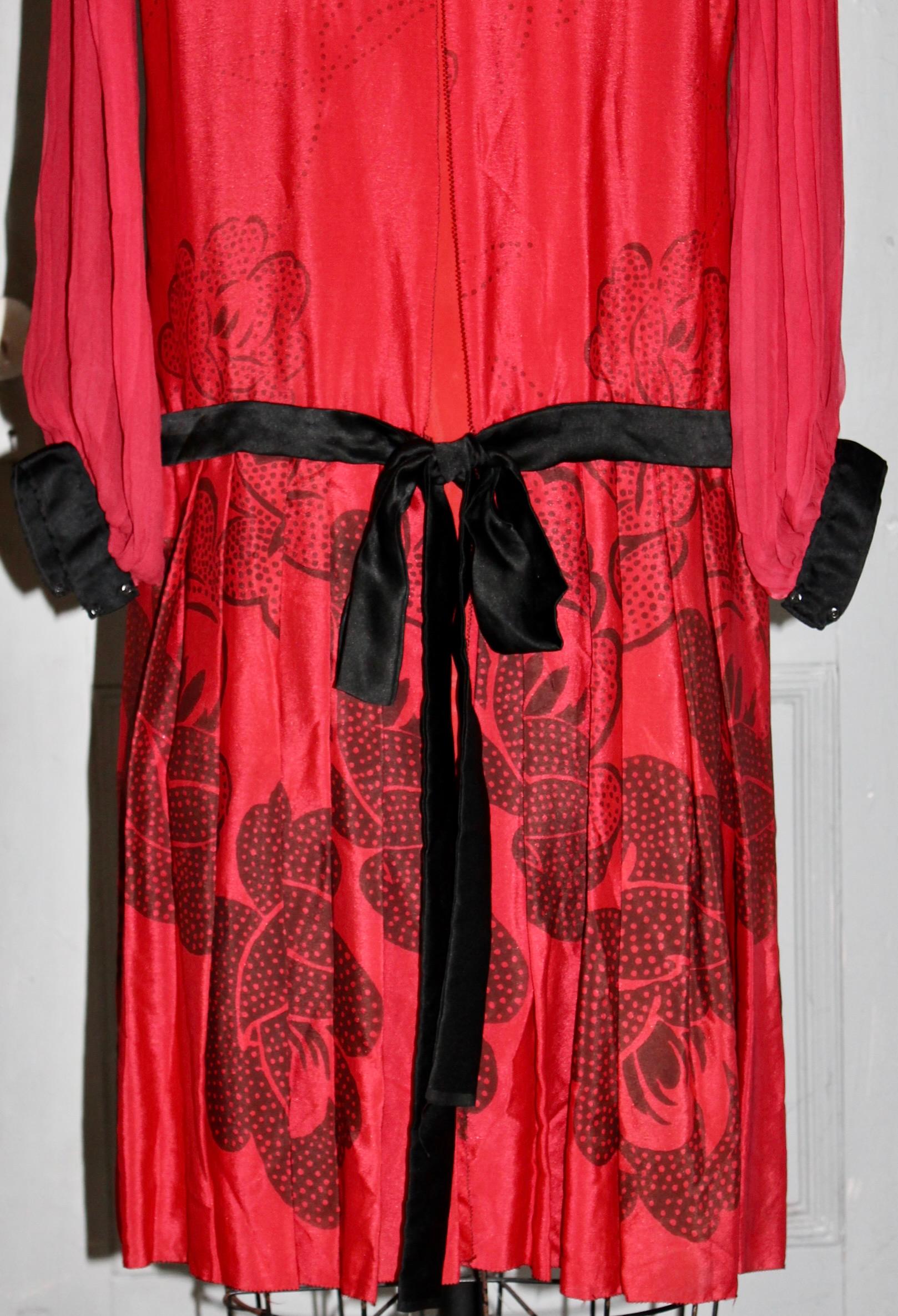 Biete ein rotes Seidenchiffon Art Deco 'Flapper' Kleid aus den 1920er Jahren im Stil von Paul
Poiret mit einem aufgedruckten schwarzen Rosenmuster in der Art von Raoul Dufy.  Plissee-Ärmel und schwarzes Samtband.  Eingenähter Beschwerungsstreifen in