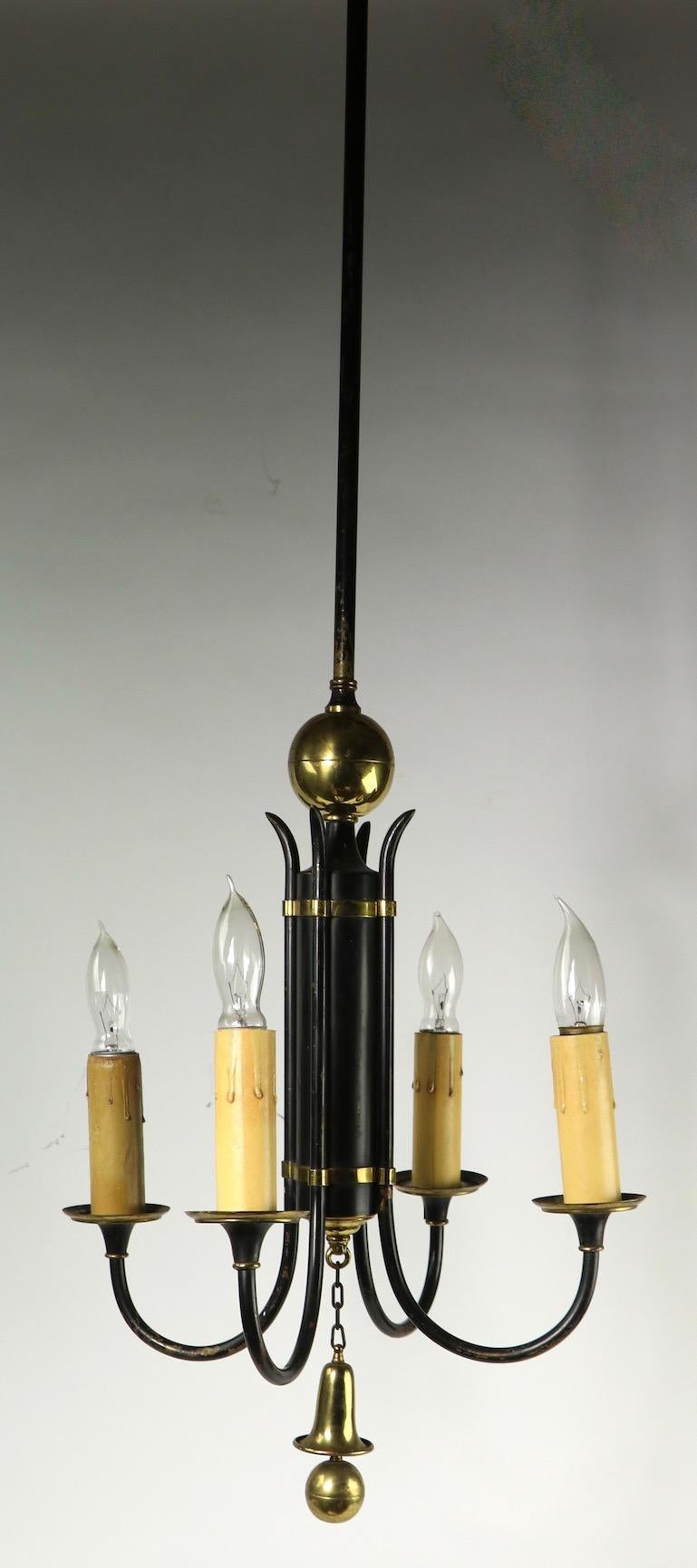 Lustre élégant à quatre lumières, en acier fini noir et garniture en laiton. Le luminaire comporte quatre douilles de bougies, fixées au corps central cylindrique. Ce lustre est en bon état, original et fonctionnel, il présente une usure cosmétique