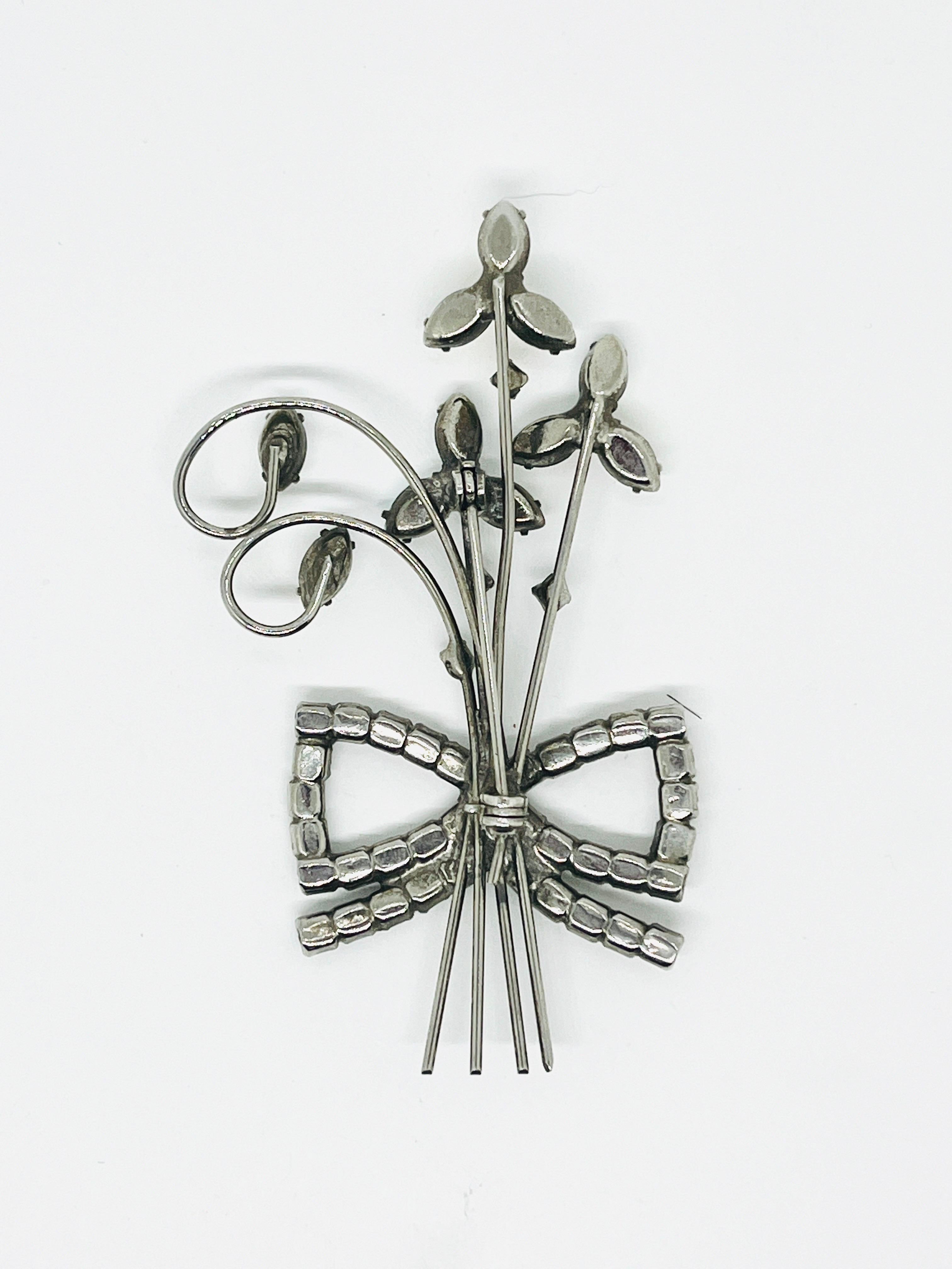 Bouquet géométrique à trois fleurs en fil de fer Art déco, avec broche en forme de noeud en strass clair, construction soudée. 

Je pense qu'il s'agit d'une pièce de la résurgence de l'Art déco du milieu du siècle, car les pierres d'aurore boréale