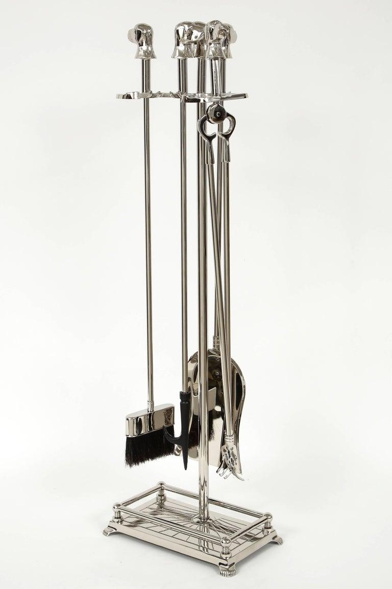 Set of Art Deco polished nickel fire tools with stylized dog head finials, most likely retriever or labrador breed. Set includes stand, shovel, poker, tongs, and broom.