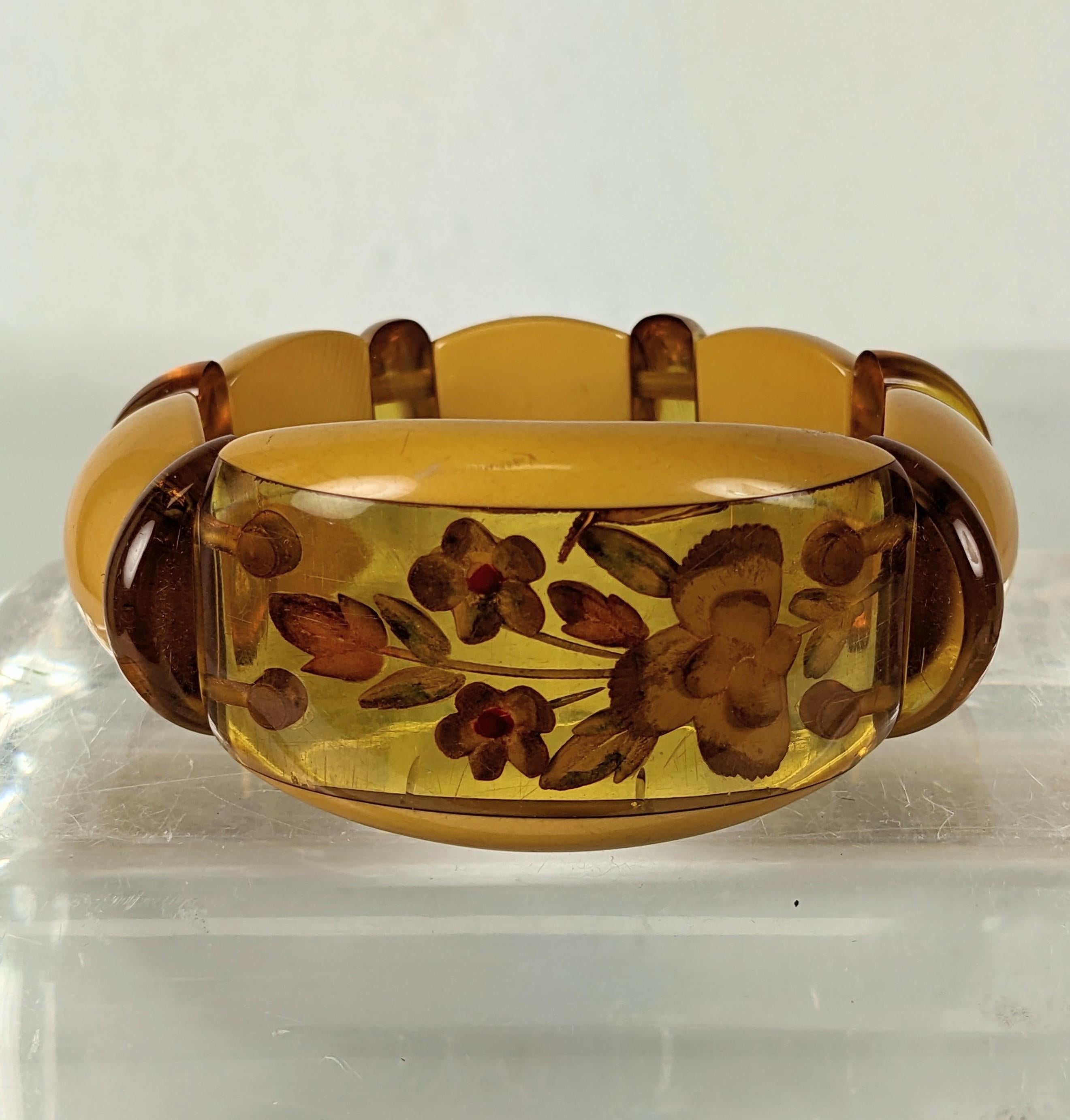 Reverse Carved Bakelite Stretch Bracelet from the Art Deco Period. Central reverse carved motif with apple juice and mango bakelite links on elastic string. Reverse carved and painted flowers on central panel. There are 3 stress cracks visible but