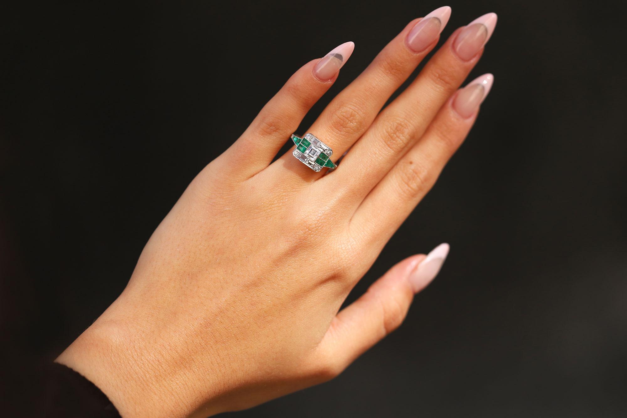 A unique engagement ring with a sleek design paying homage to the 1920s Art Deco Gatsby era, this platinum masterpiece is hand crafted around a vintage 1/2 carat carrè cut diamond. Laced with lush, green Colombian emeralds and diamonds precisely set