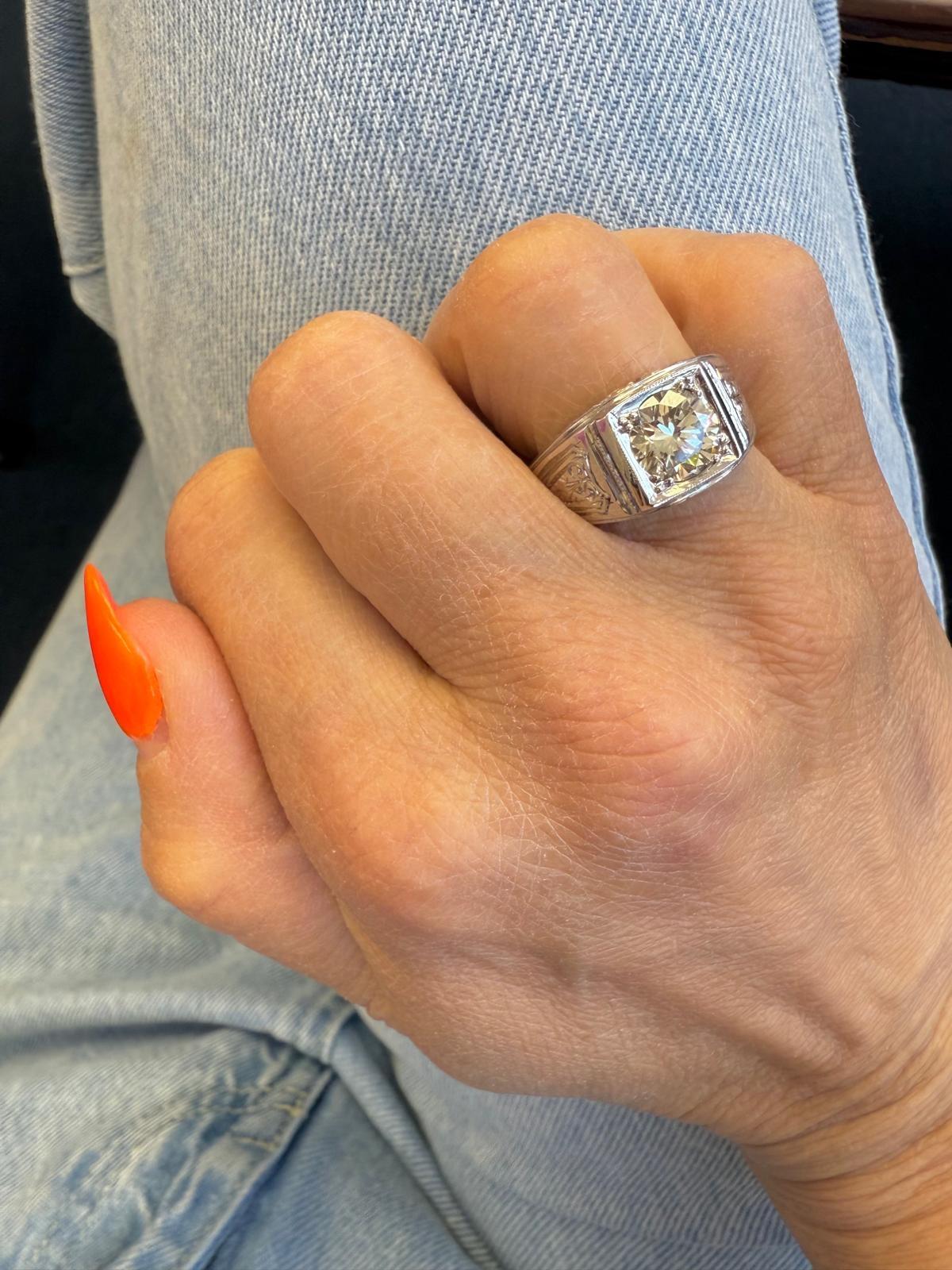 Este anillo de oro blanco de 18 quilates, una declaración audaz y atemporal, presenta un diamante central redondo de talla brillante de aproximadamente 1,68 quilates. Engarzado en un bisel cuadrado con delicados bordes milgrain y flanqueado por