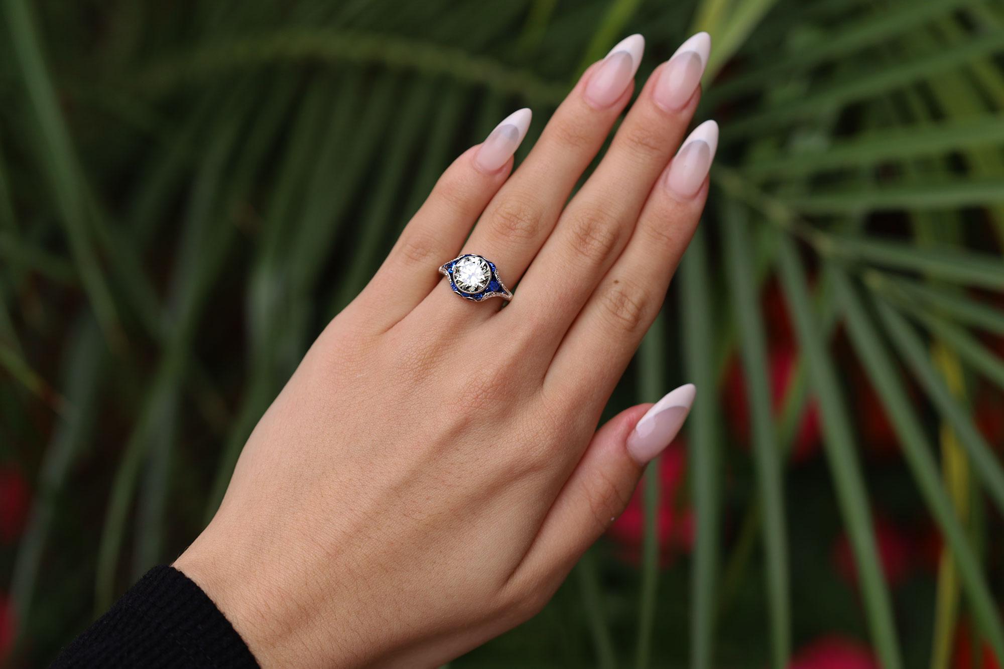 A wonderful Art Deco inspired 2.34 carat diamond and sapphire engagement ring. With a sizzling scintillation, the round brilliant diamond sparkles with life and fire. The bespoke platinum mounting is adorned with French and calibré cut velvety blue