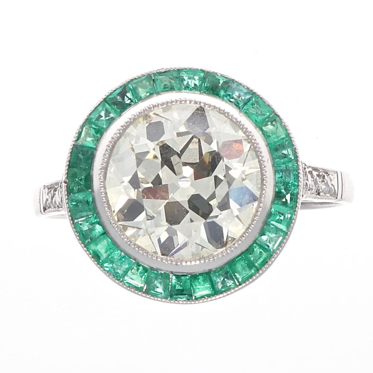 Everlasting beauty symbolizing eternal love through conventional design. Featuring an approximately 2.50 carat old European cut diamond that is  M color, VS clarity. Surrounded by a ring of glowing green emeralds. Crafted in platinum. Ring size 7