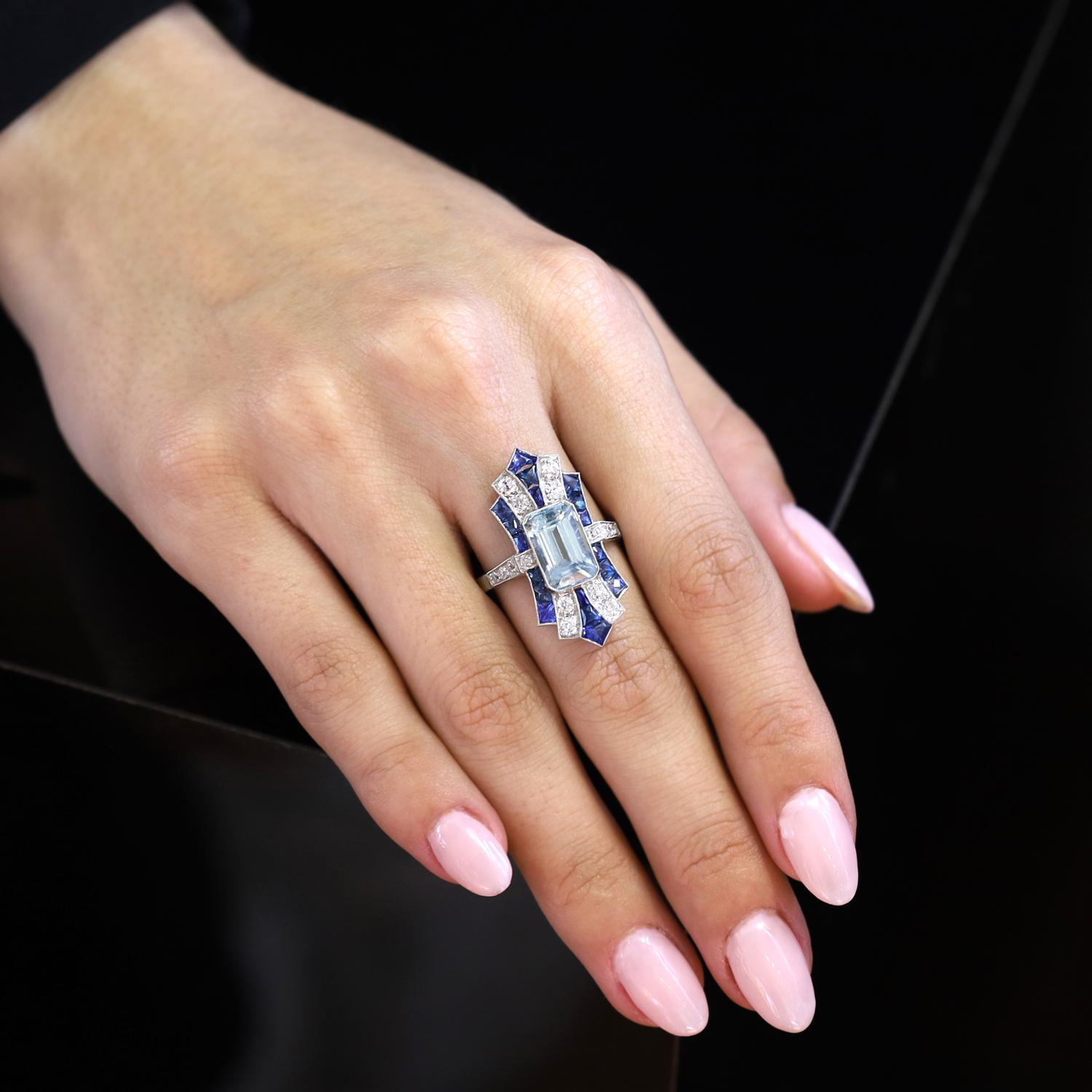 Este espectacular anillo de cóctel deslumbra como ningún otro. La aguamarina alargada central de 3.16 quilates está exquisitamente tallada para resaltar un brillante azul marino rodeado de haces de ricos zafiros azules talla francesa y calibré y