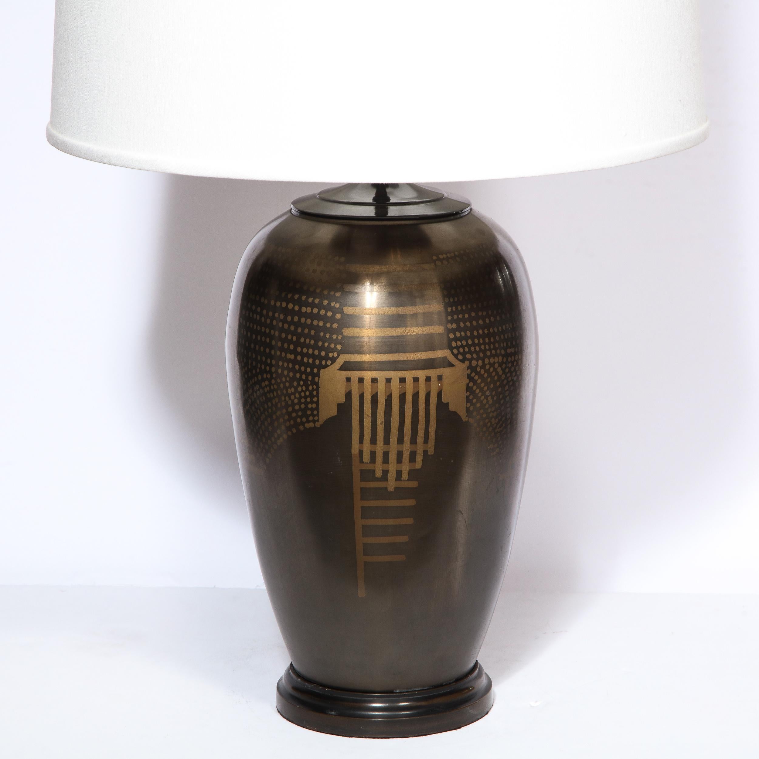 This stunning Art Deco revival table lamp was realized in the United States during the latter half of the 20th century. It features a beveled bronze circular base and a tiered skyscraper style neck. The sinuously curved body is replete with a wealth