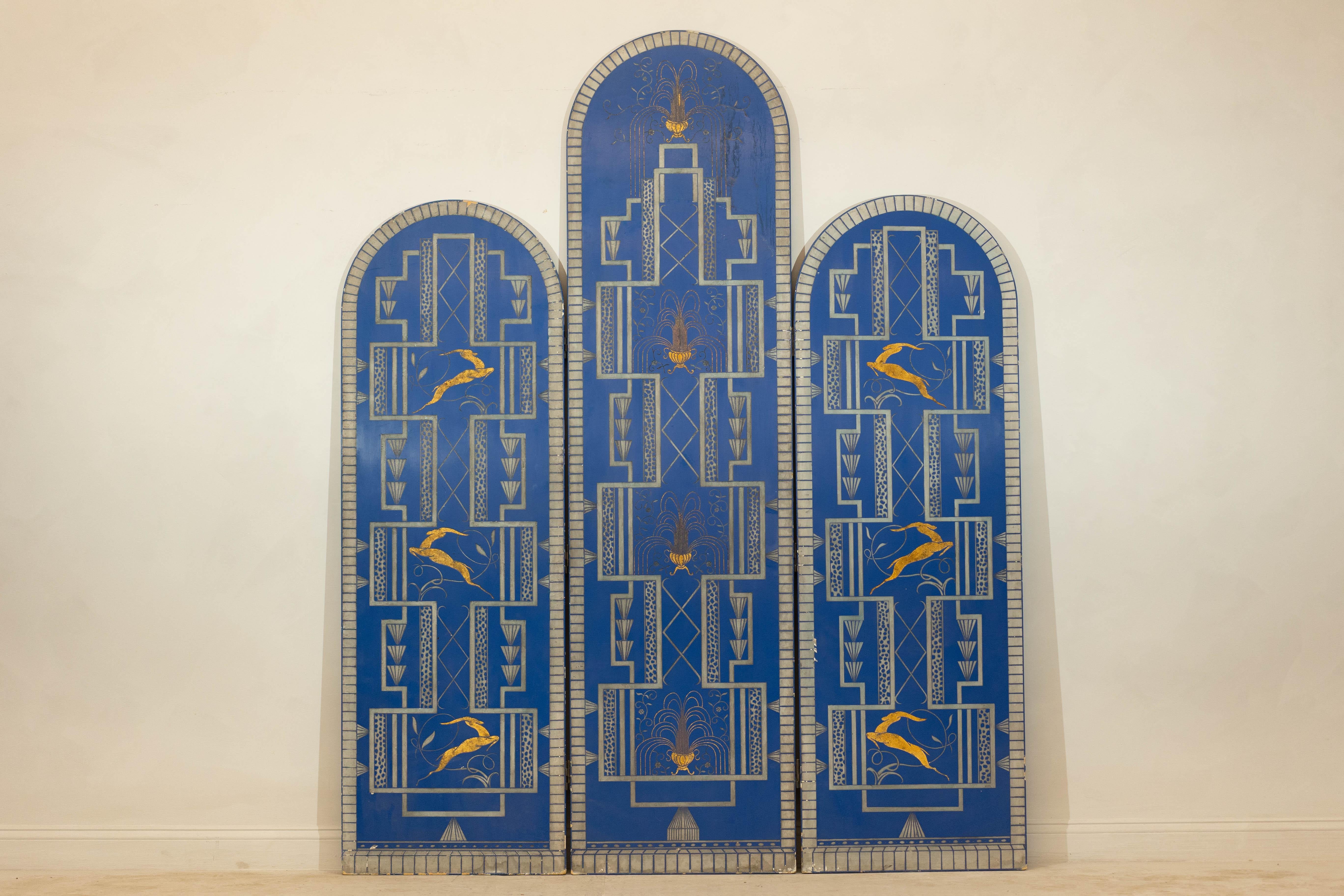 An Art Deco Revival cobalt blue three-panel arched screen with gilded gazelles. Boldly embracing the glamour of the Art Deco revival, this exquisite three-panel folding screen captivates with its vivid cobalt blue backdrop adorned with gilded