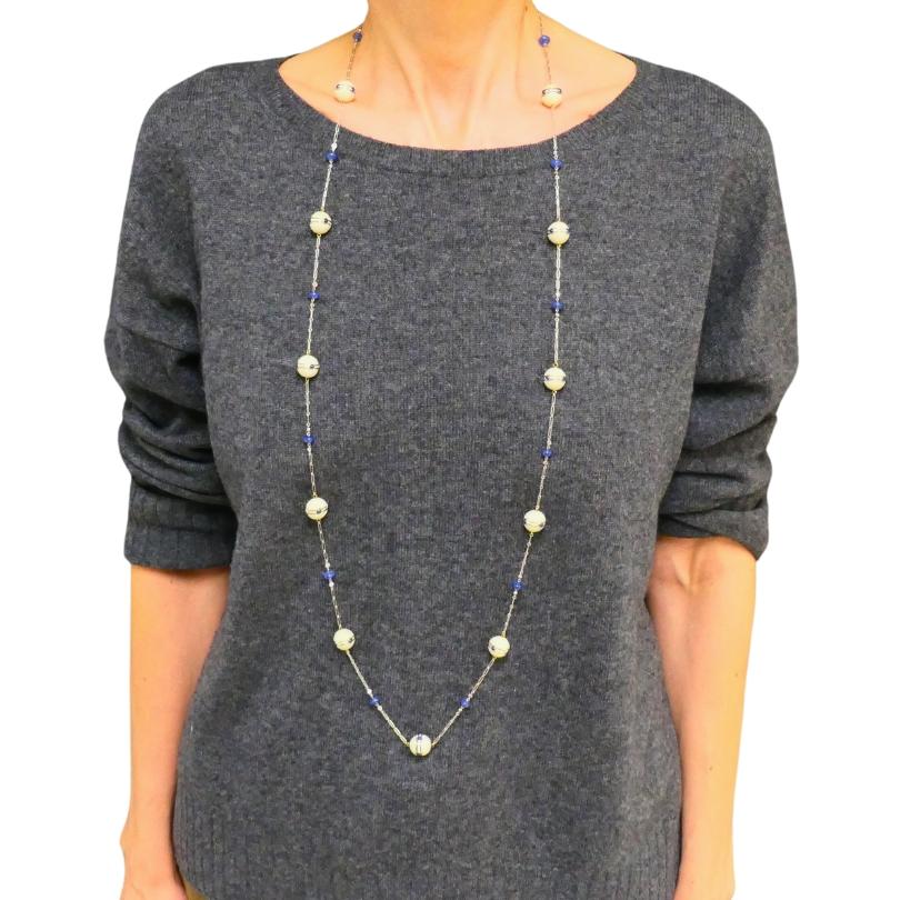 Delicata collana a catena in platino in stile Art Déco, con perle smaltate, zaffiri e diamanti.
La catena in platino è dotata di perline smaltate, che mostrano i toni cremosi delle perle e si alternano a sognanti rondelle di zaffiro blu. Ogni