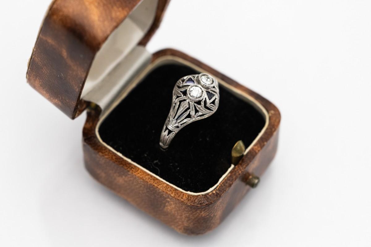 An old white gold ring with old-cut diamonds and synthetic sapphires. This ring is made of white gold, which was a popular choice in the Art Deco style for its modernity and elegance. White gold provides a background for diamonds and sapphires,