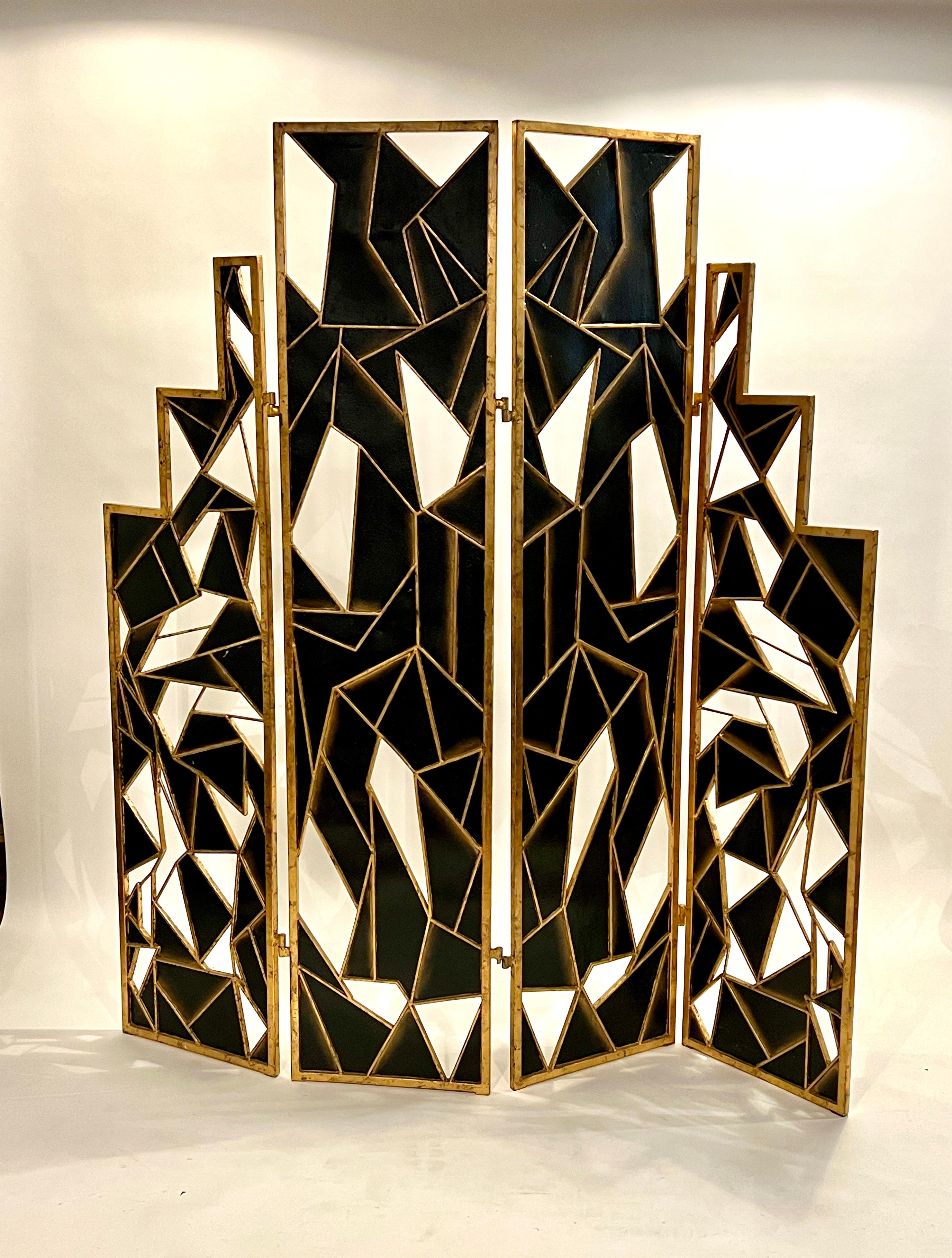20th century art deco room divider crafted in a patina gold painted metal frame with black painted abstract panels and cut out windows. 4 panel screen can be separated by hook attachments and shows identical images on front and back, 