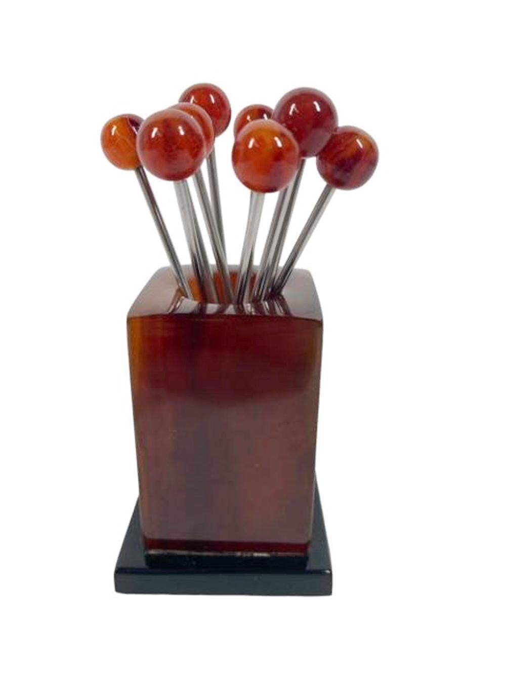 Set of ten translucent root beer Bakelite ball topped cocktail picks in a tall block stand of swirled root beer Bakelite on a black Bakelite plinth base.