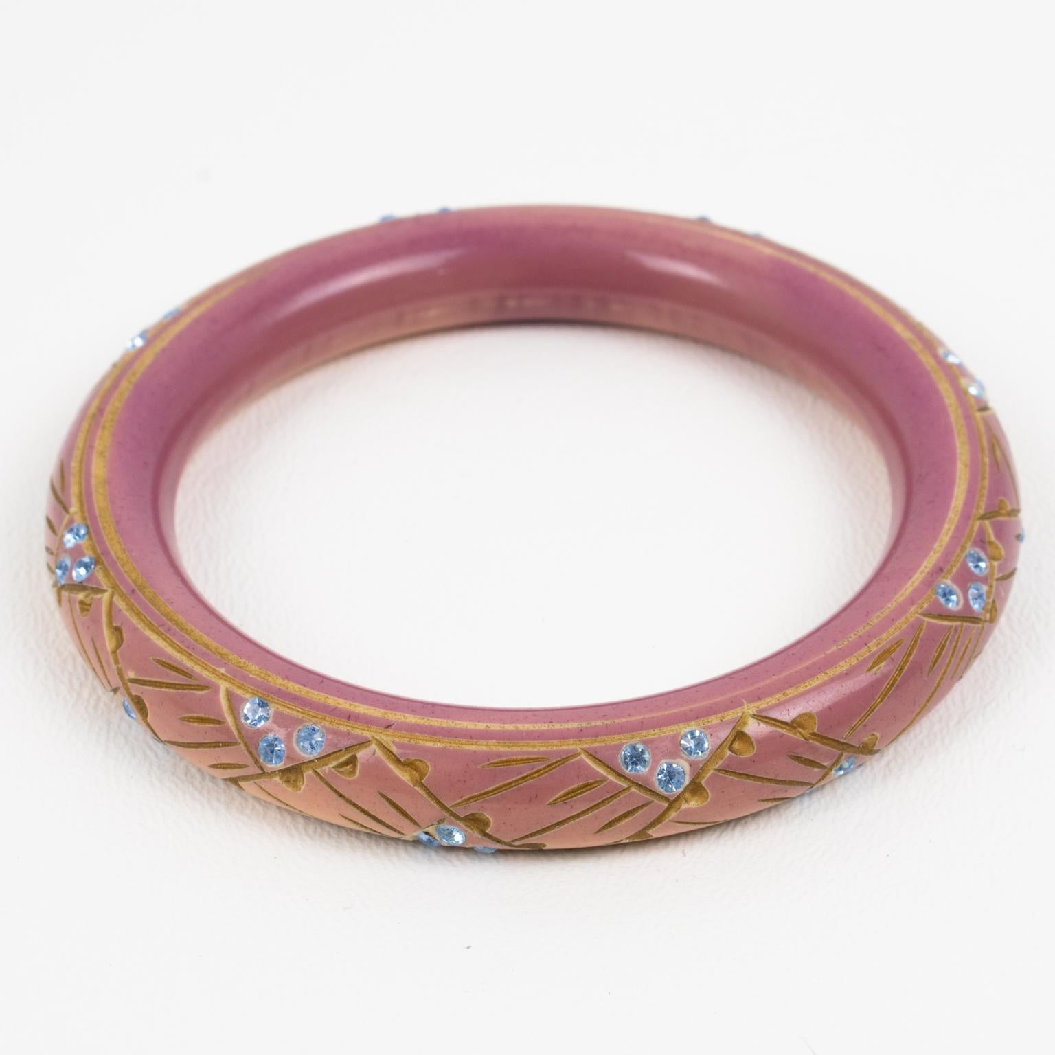 This lovely French Art Deco Galalith bracelet bangle boasts a geometric carved design, contrasted with gold paint application and complimented with baby blue crystal rhinestones. The piece has a tube shape and a superb rose beige color with an