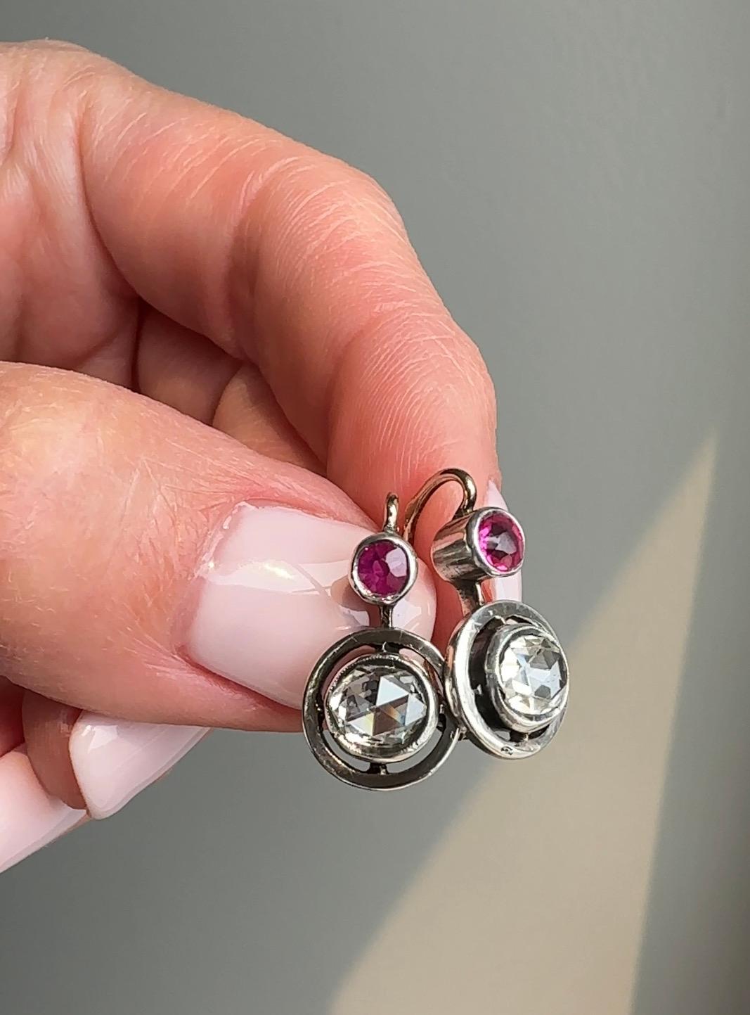 A pair of glittering rose-cut diamonds float from within silver topped 14k gold halos suspended below vibrant rubies. 

 

Diamonds: estimated .60 ct each, SI1 clarity with I-J range in color

Ruby: estimated .13 ct each

Measurements: 3/4