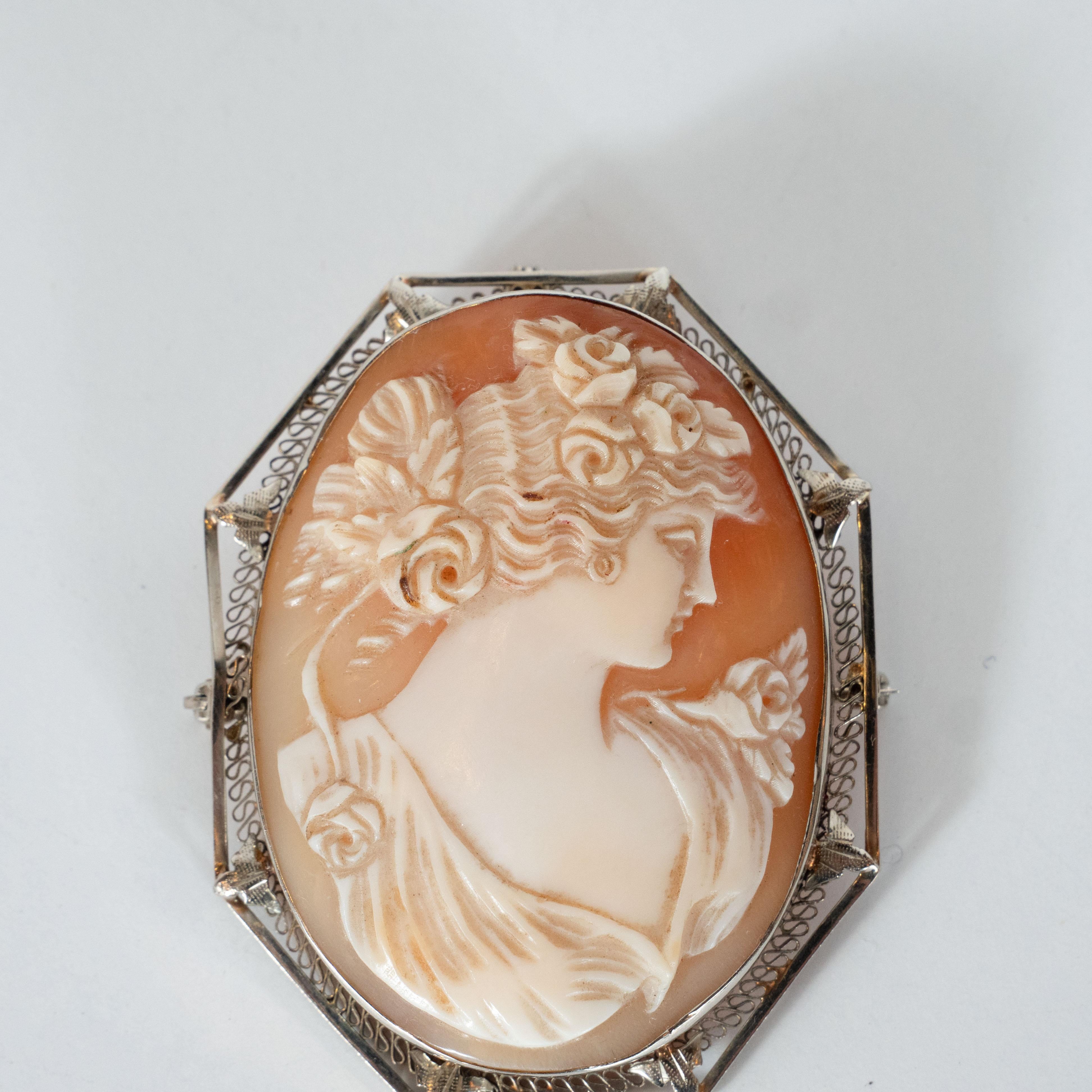 This gorgeous Art Deco cameo was realized in the United States, circa 1925. It features an oval charm of a stylized lady presented in relief in white shell carved against an ombre rose shell background. The beautiful female figure has flowing curly