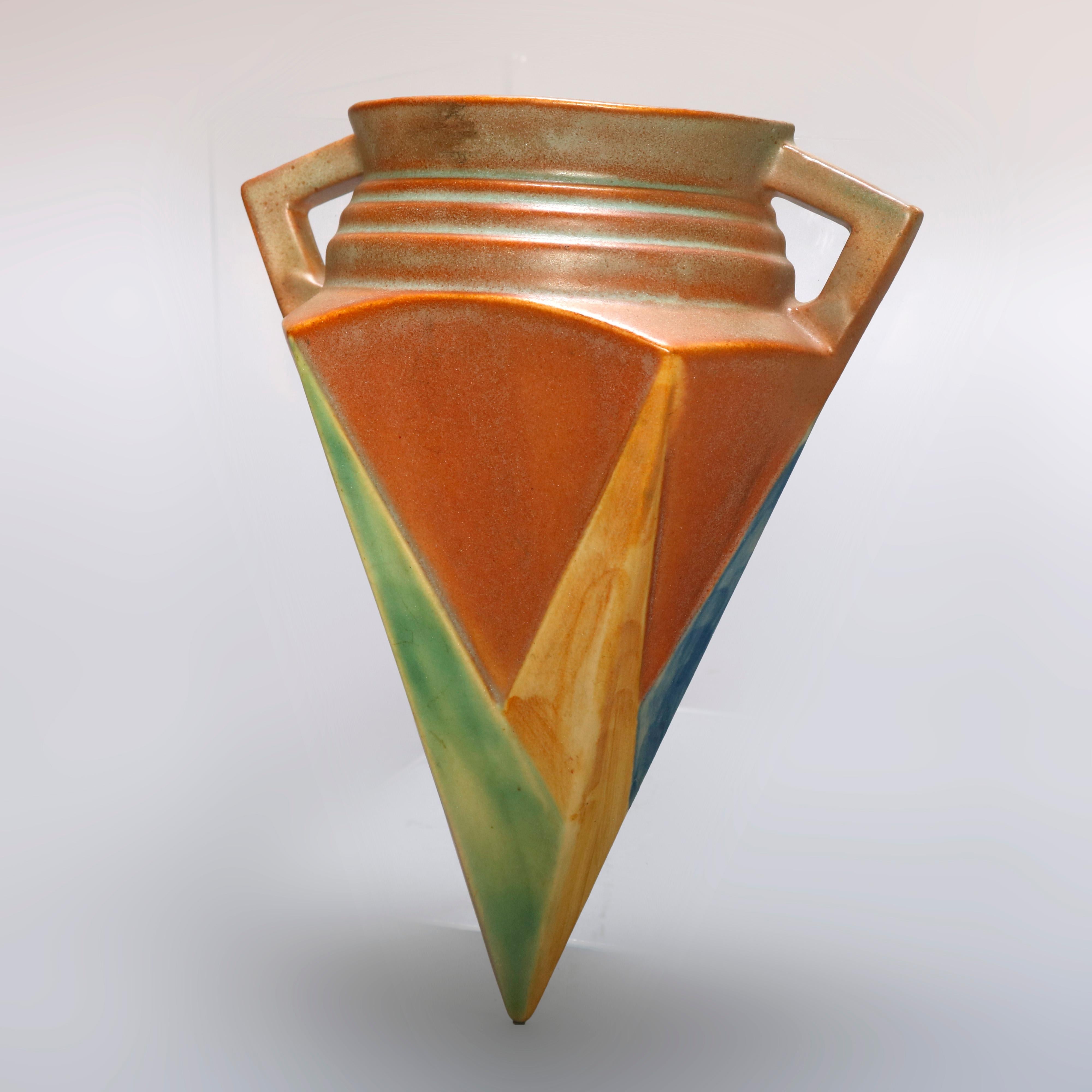 A vintage Art Deco wall pocket in the Futural line by Roseville Art Pottery offers stylized urn form with polychromed and faceted base with double handles, en verso original label as photographed, circa 1930.

Measures: 8.25