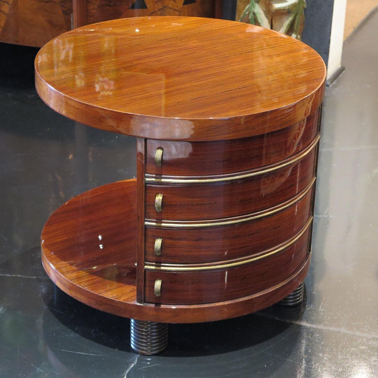 This unusual Art Deco side table features a rounded frame in rosewood with a high gloss finish. Along one side of the body are four small drawers that fan out in a triangular fashion with the original antique brass hardware. The other side of the