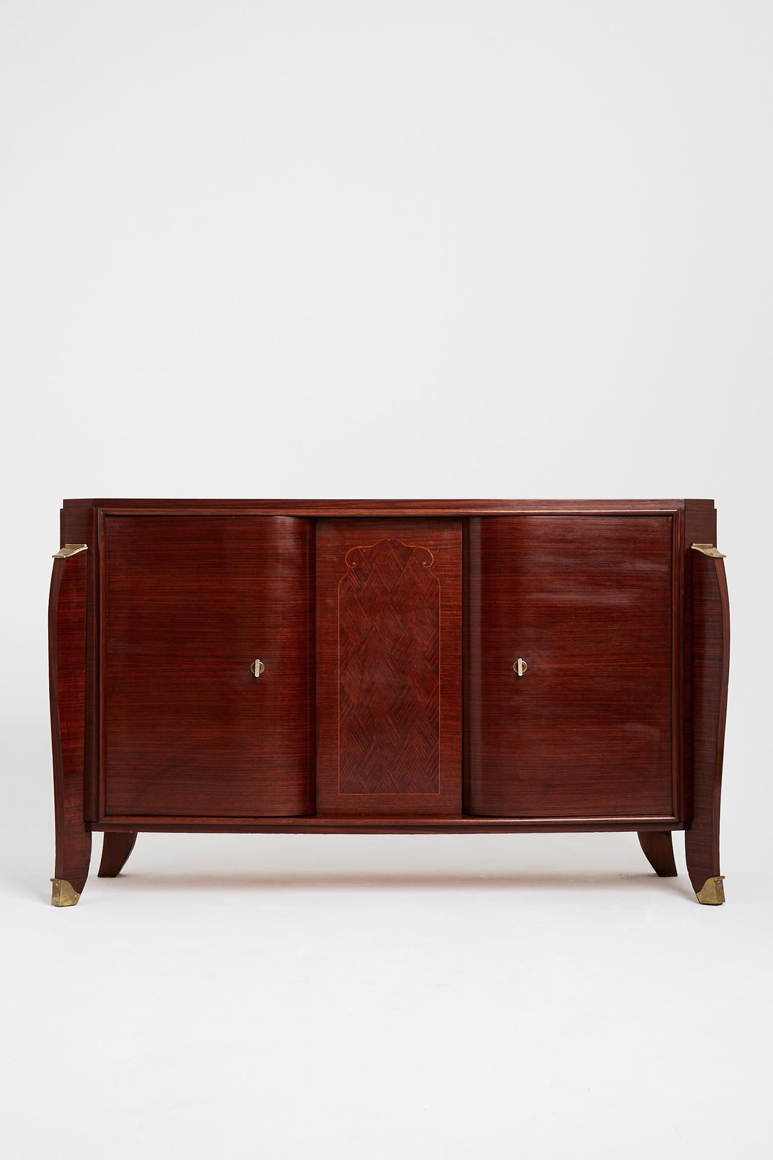 An Art Deco mahogany sideboard by Jules Leleu (1883-1961), the two curved doors centered by a diamond patterned marquetry, on sabre legs with bronze mounts, internally veneered in sycamore, with two adjustable shelves.
France, circa 1935.